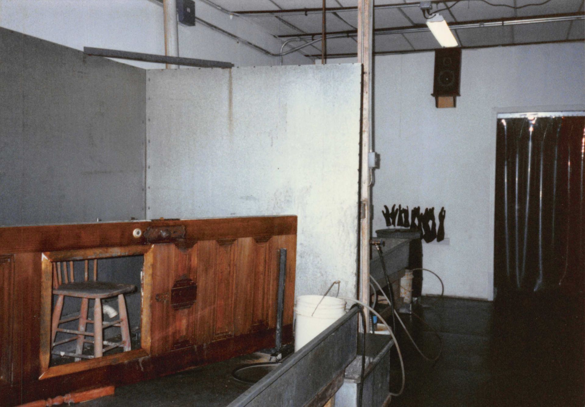 An interior view of a workshop with a wooden booth, equipment, and a hanging speaker.