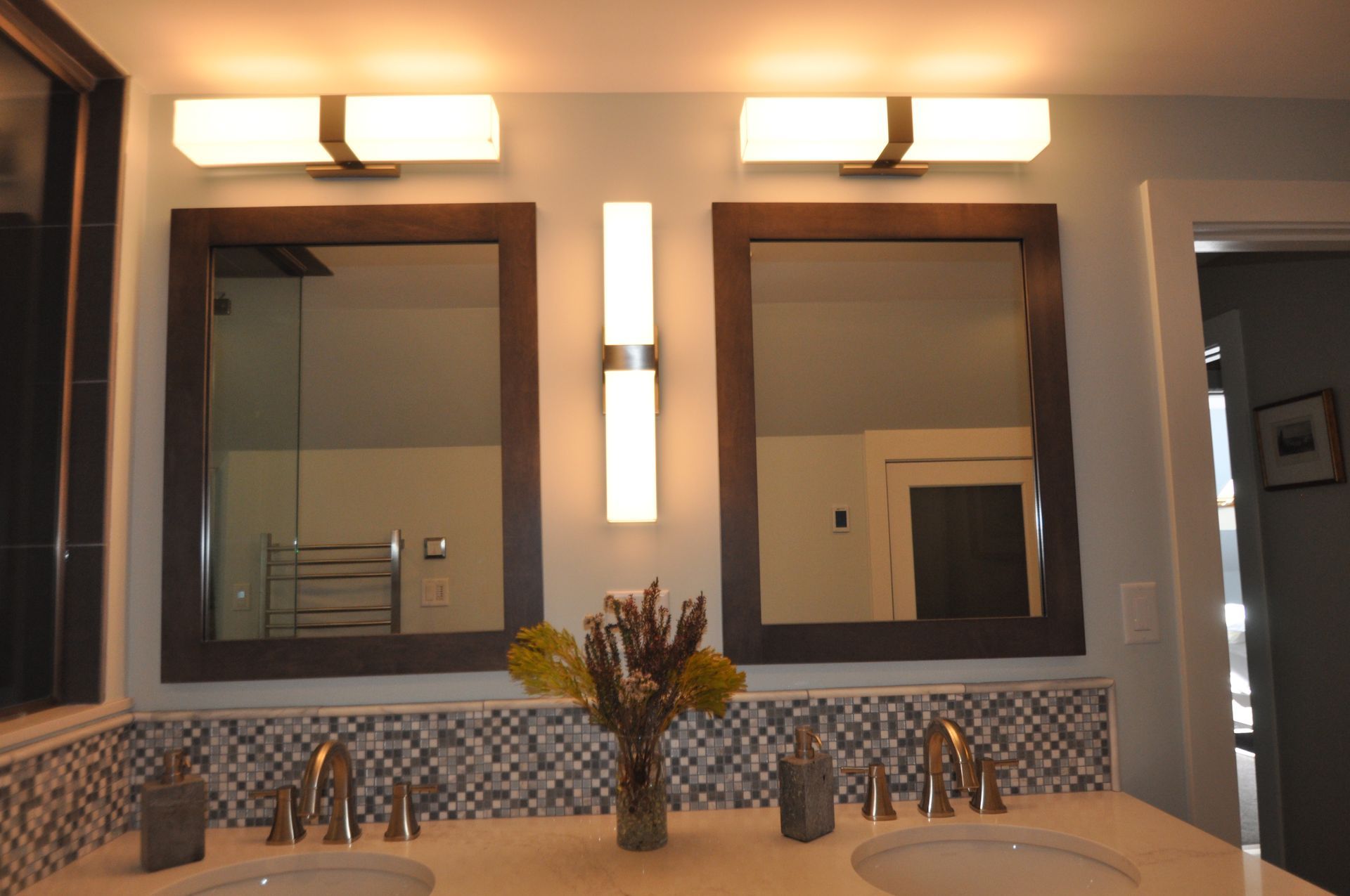 Bathroom with two mirrors, sinks, and lights. Features a mosaic tile backsplash and brown-framed mirrors.