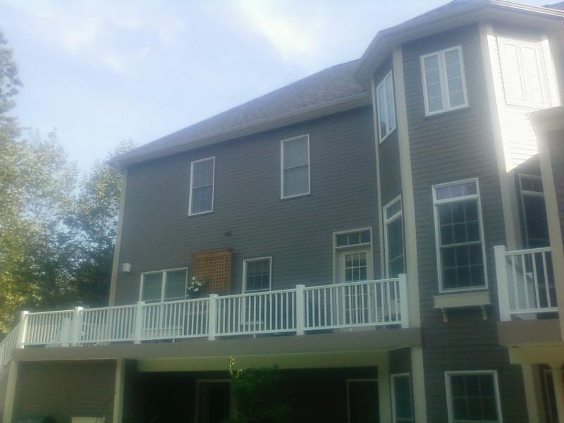 Two-story gray house with white deck and railings. Sunny outdoor setting.