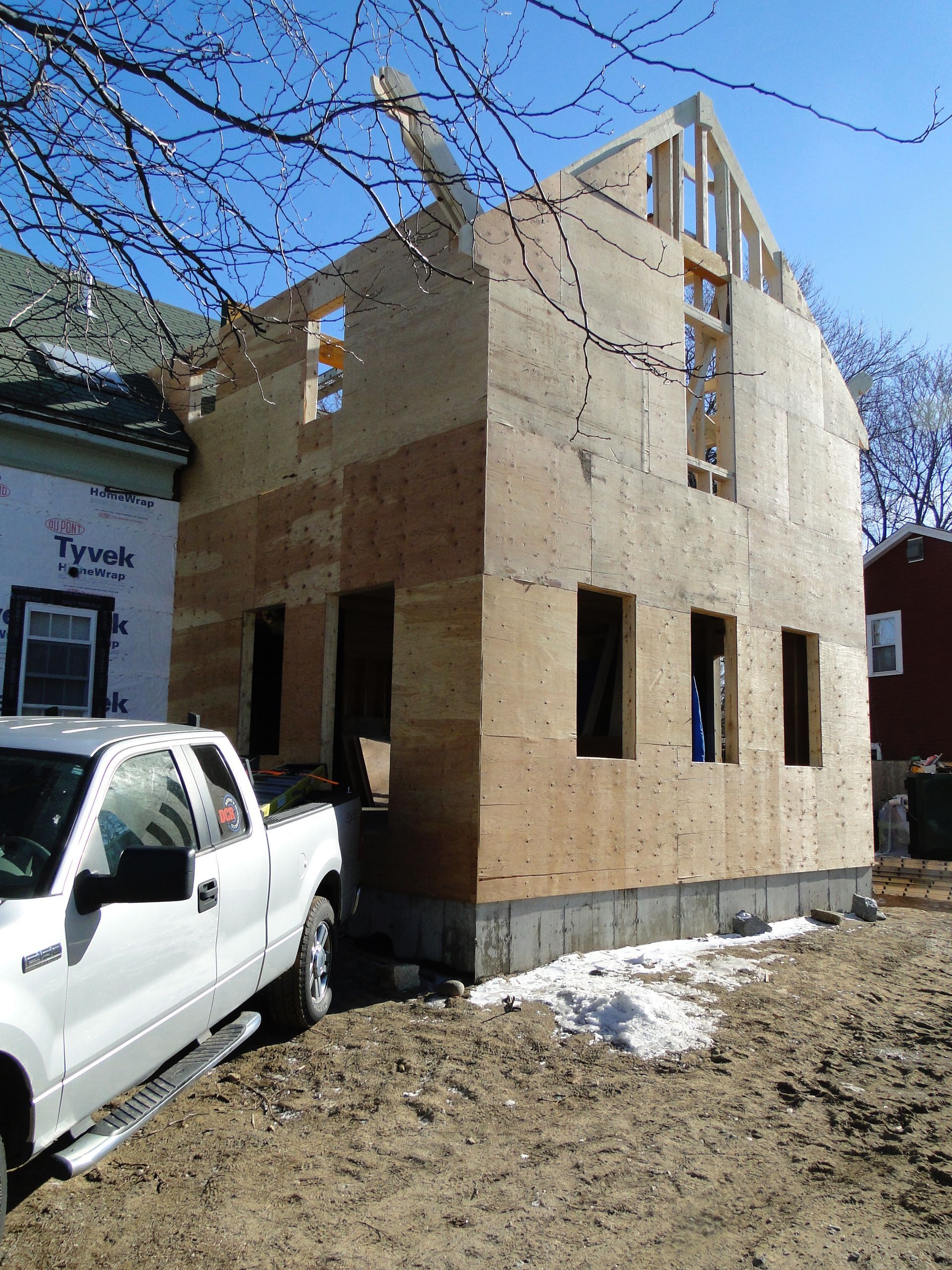 New house construction with plywood walls and a white pickup truck in front.
