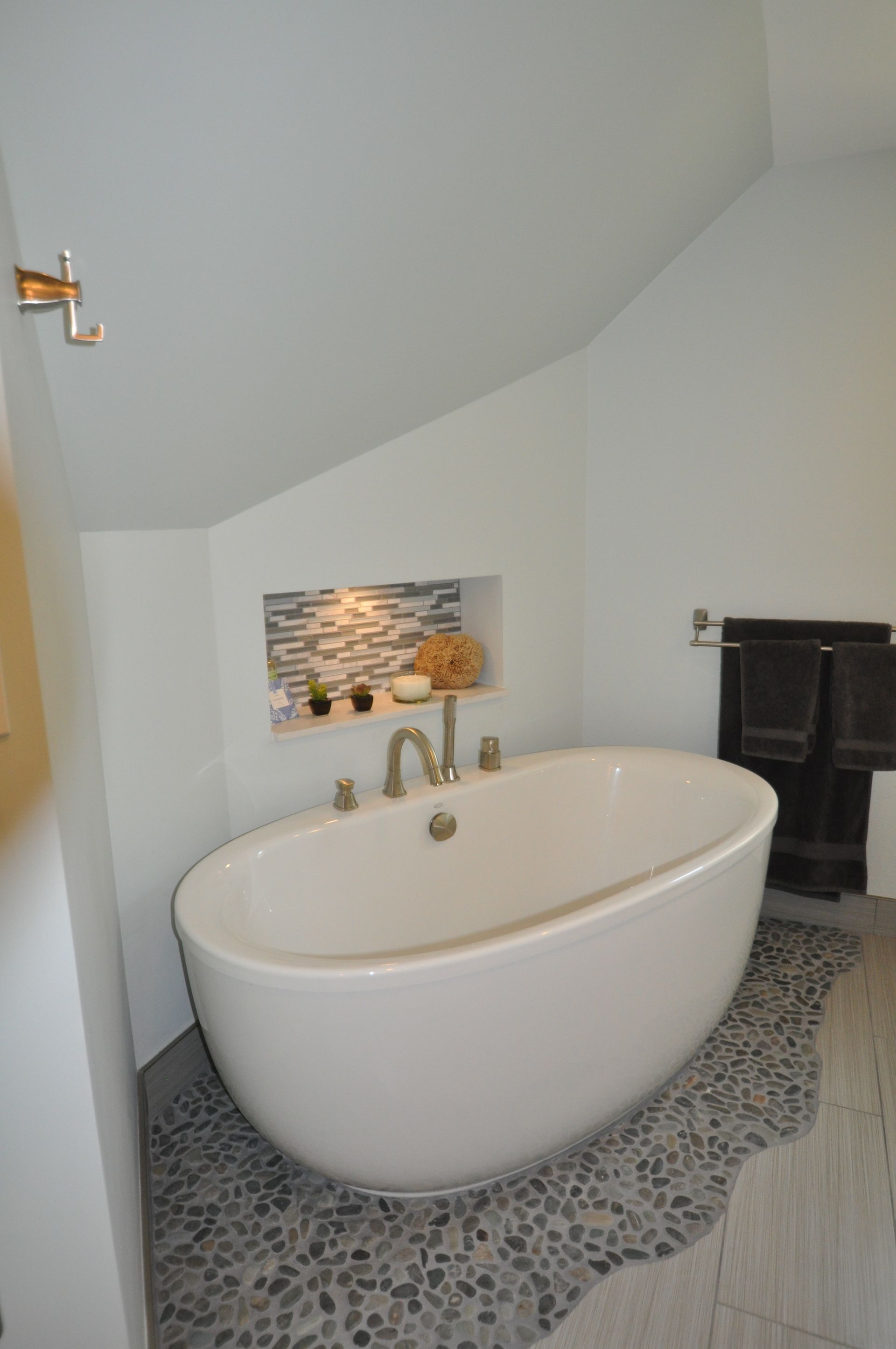 Modern bathroom with a white oval bathtub, pebble floor, and recessed shelf.
