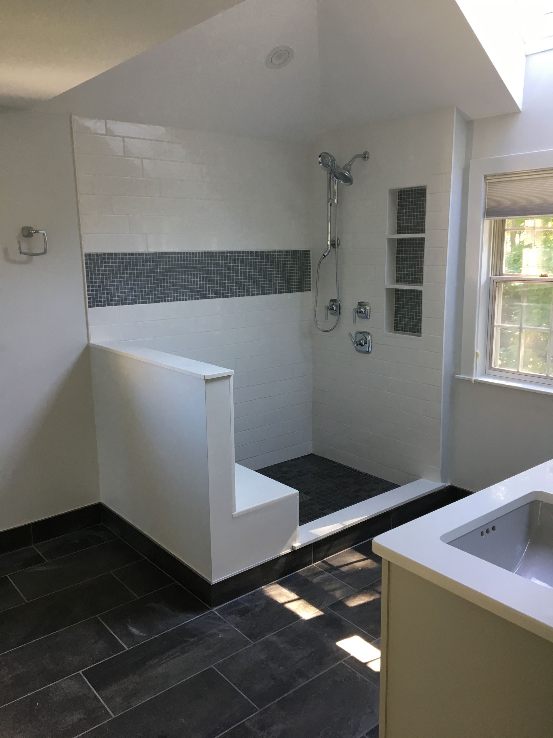 Modern bathroom with walk-in shower, gray tile floor, white walls, and a small window.