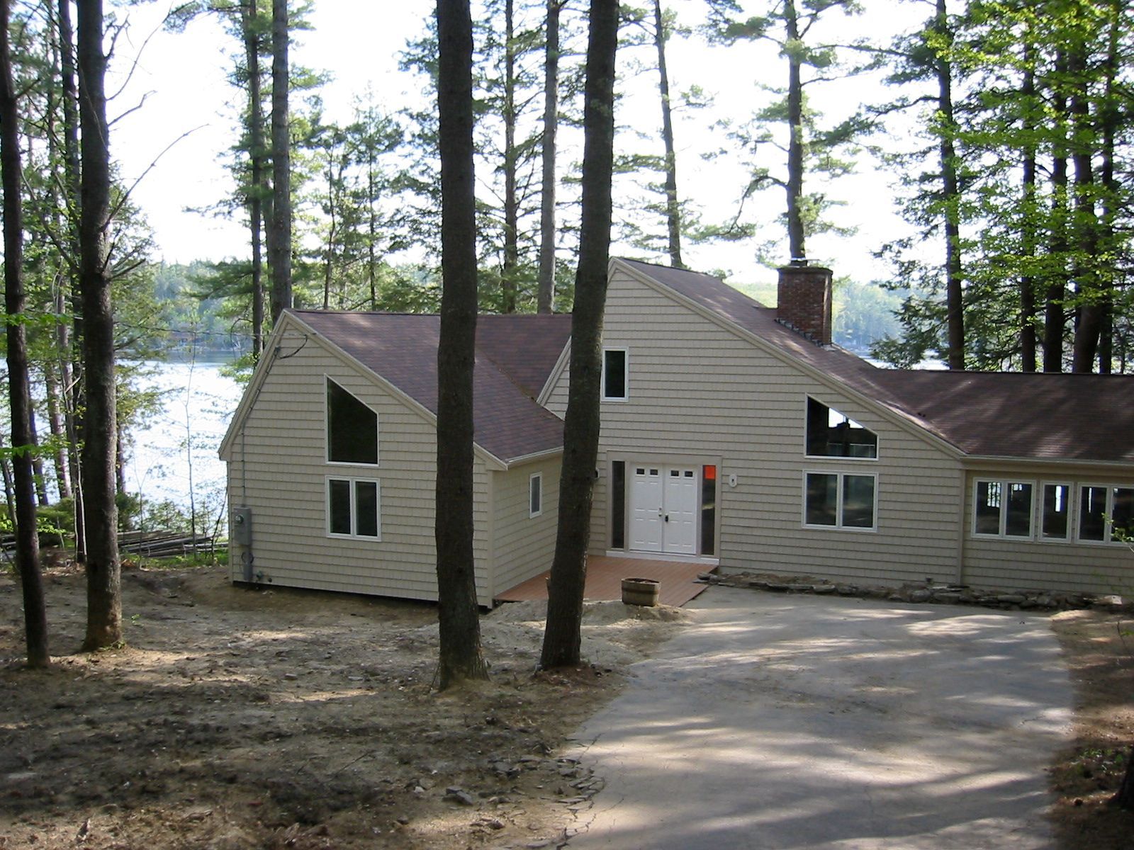 Beige house with large windows, driveway, trees, and a lake in the background.