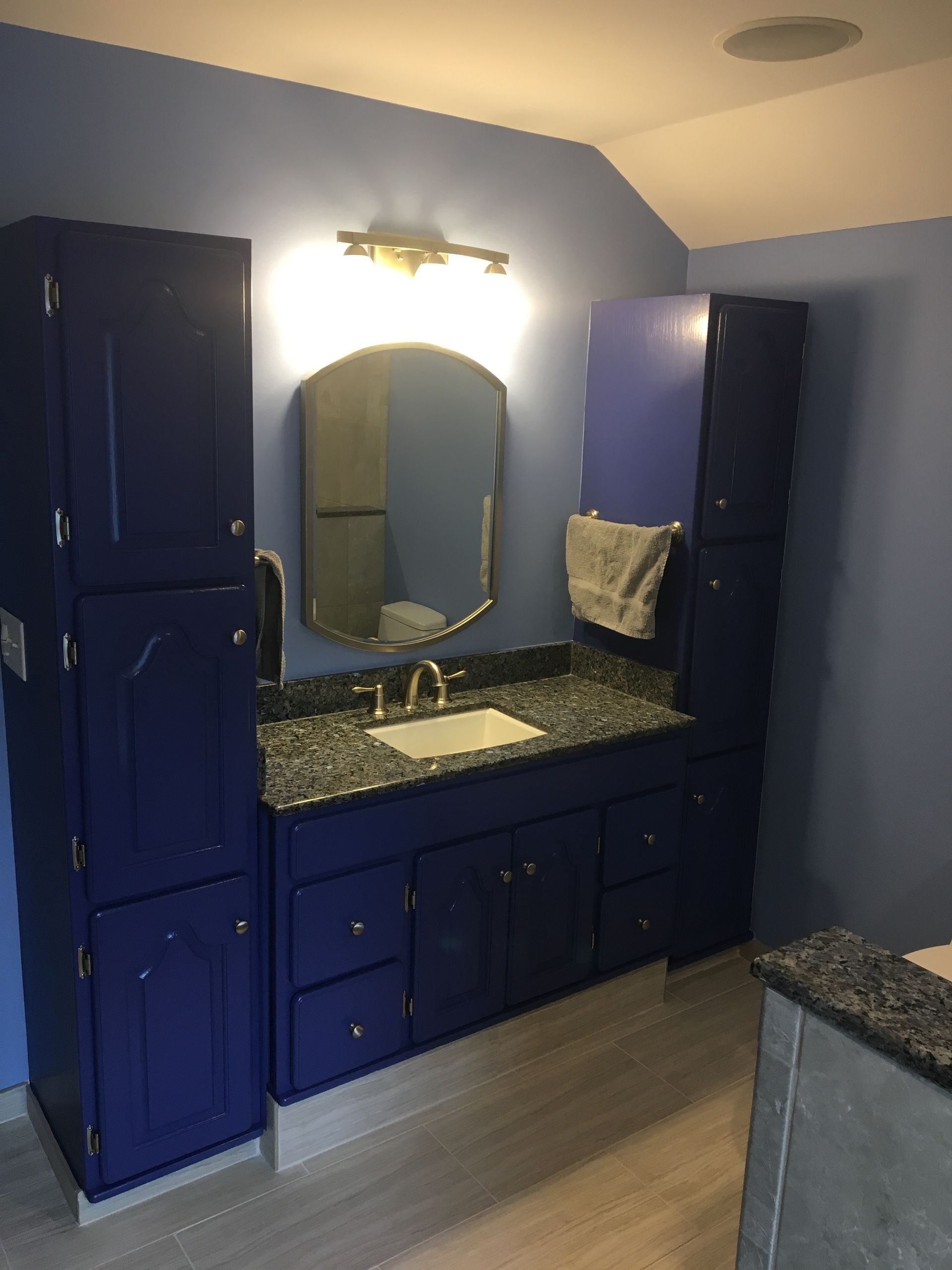 Bathroom with blue cabinets, granite countertop, mirror, and light fixture.