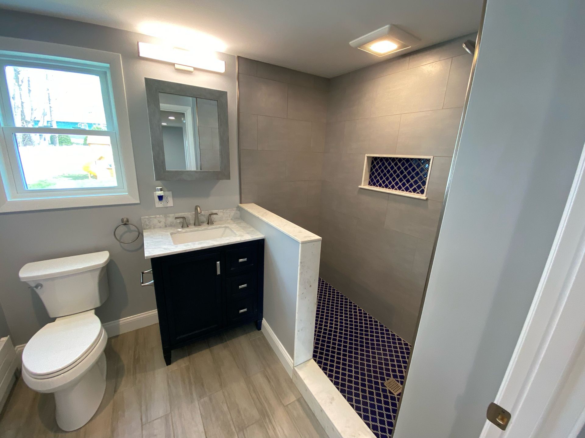 Bathroom with gray walls, dark blue vanity, and a walk-in shower with blue tiled floor.