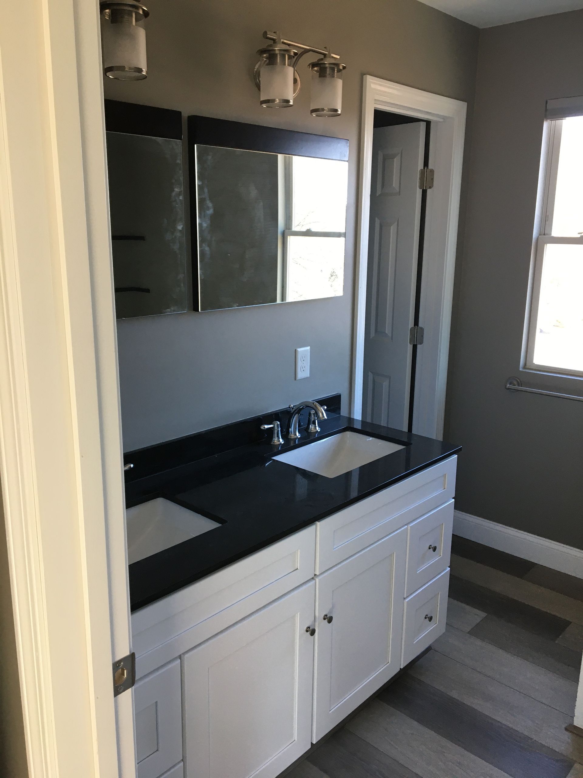 White double-sink vanity with black countertop, mirrors, and lighting in a bathroom with gray walls.