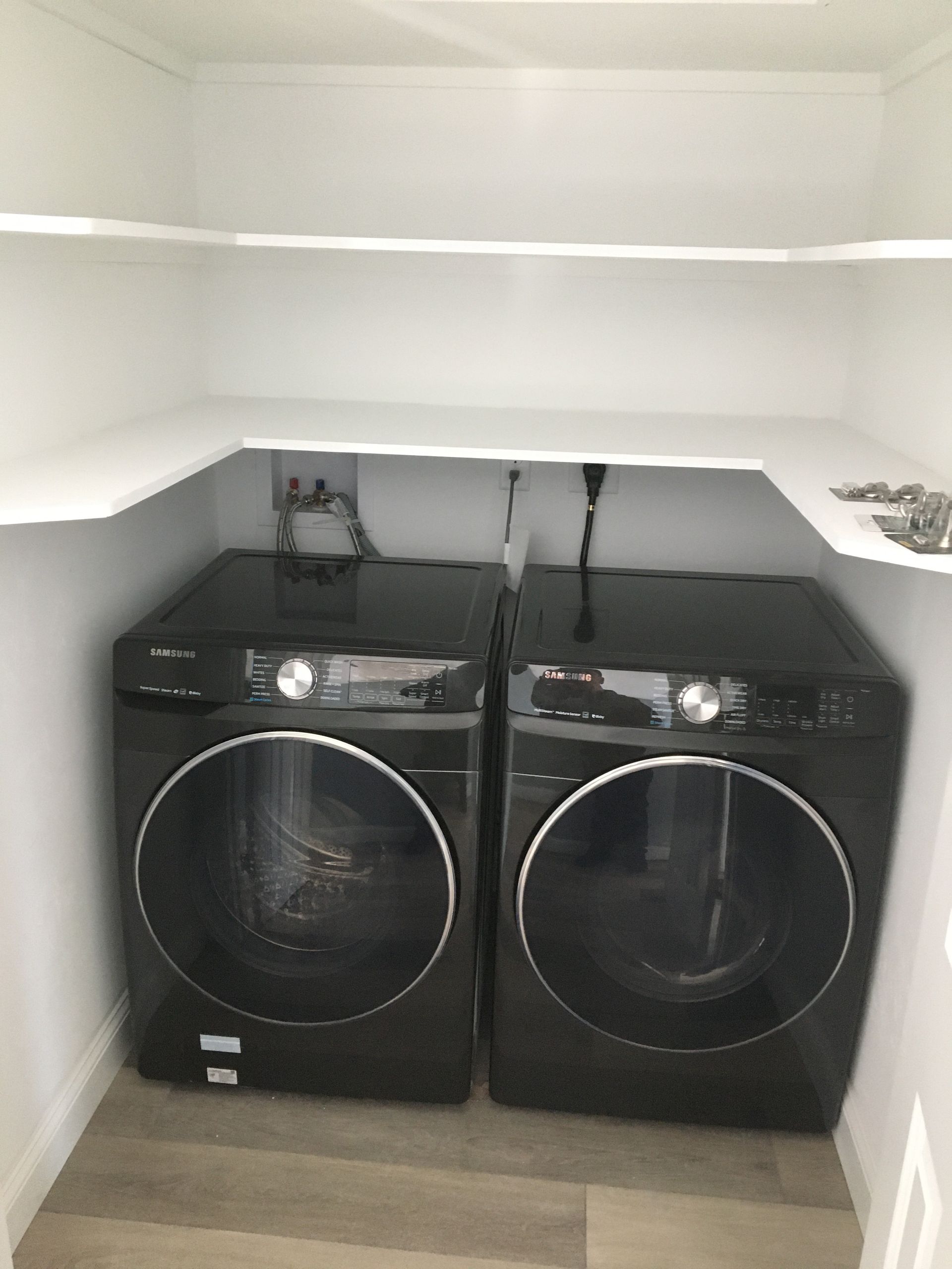 Black washer and dryer set in a small laundry closet with white shelves.