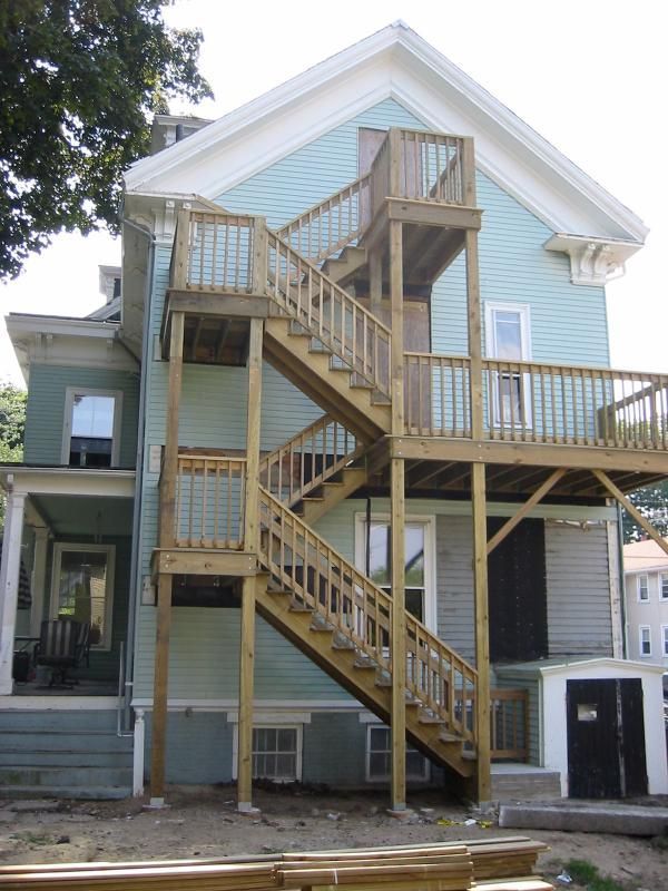 Two-story house with exterior wooden staircases and decks painted blue-green.