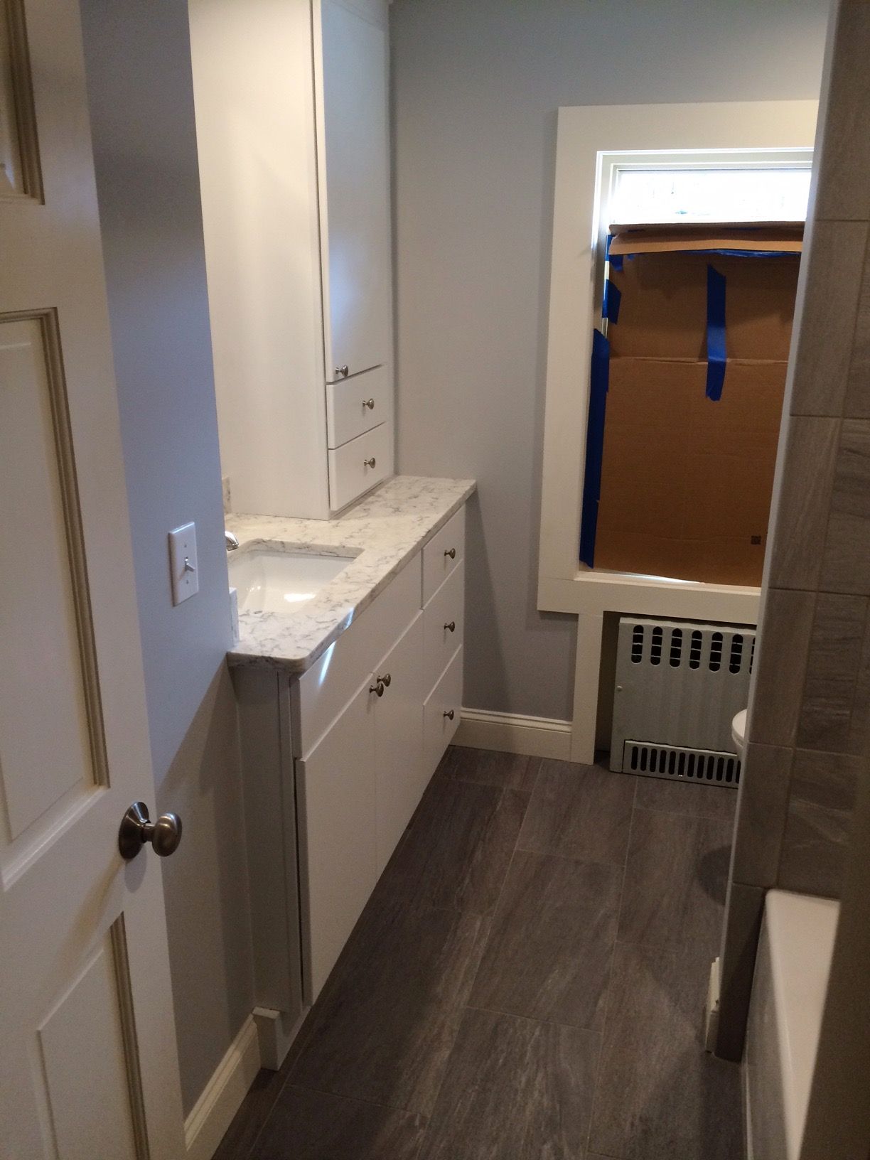 Bathroom with white cabinets, gray walls, and wood-look flooring; unfinished window; light-colored countertop.