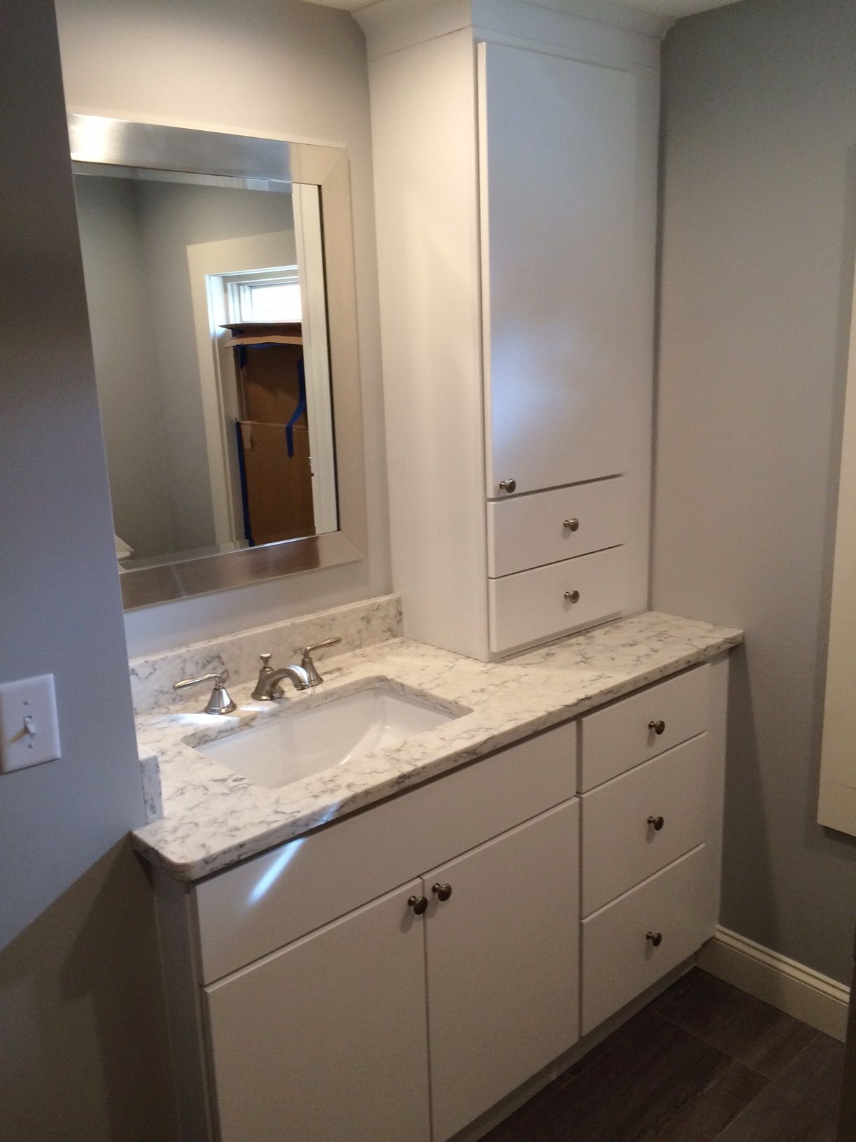 White bathroom vanity with sink, mirror, and storage cabinet. Granite countertop, gray walls.