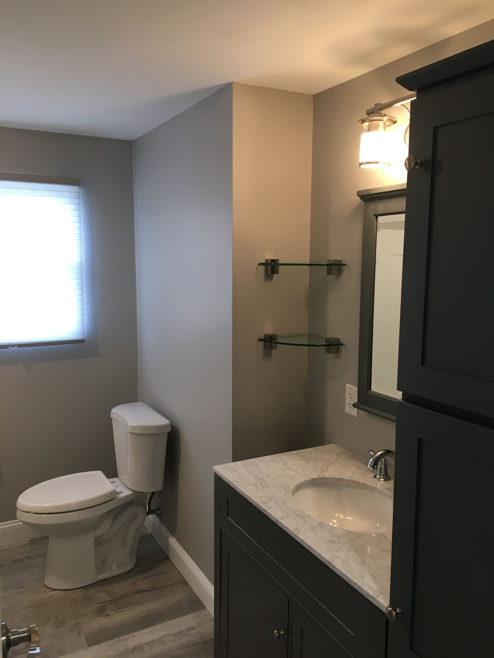 Bathroom with a toilet, sink, vanity, mirror, and storage cabinet. Gray walls and floor.