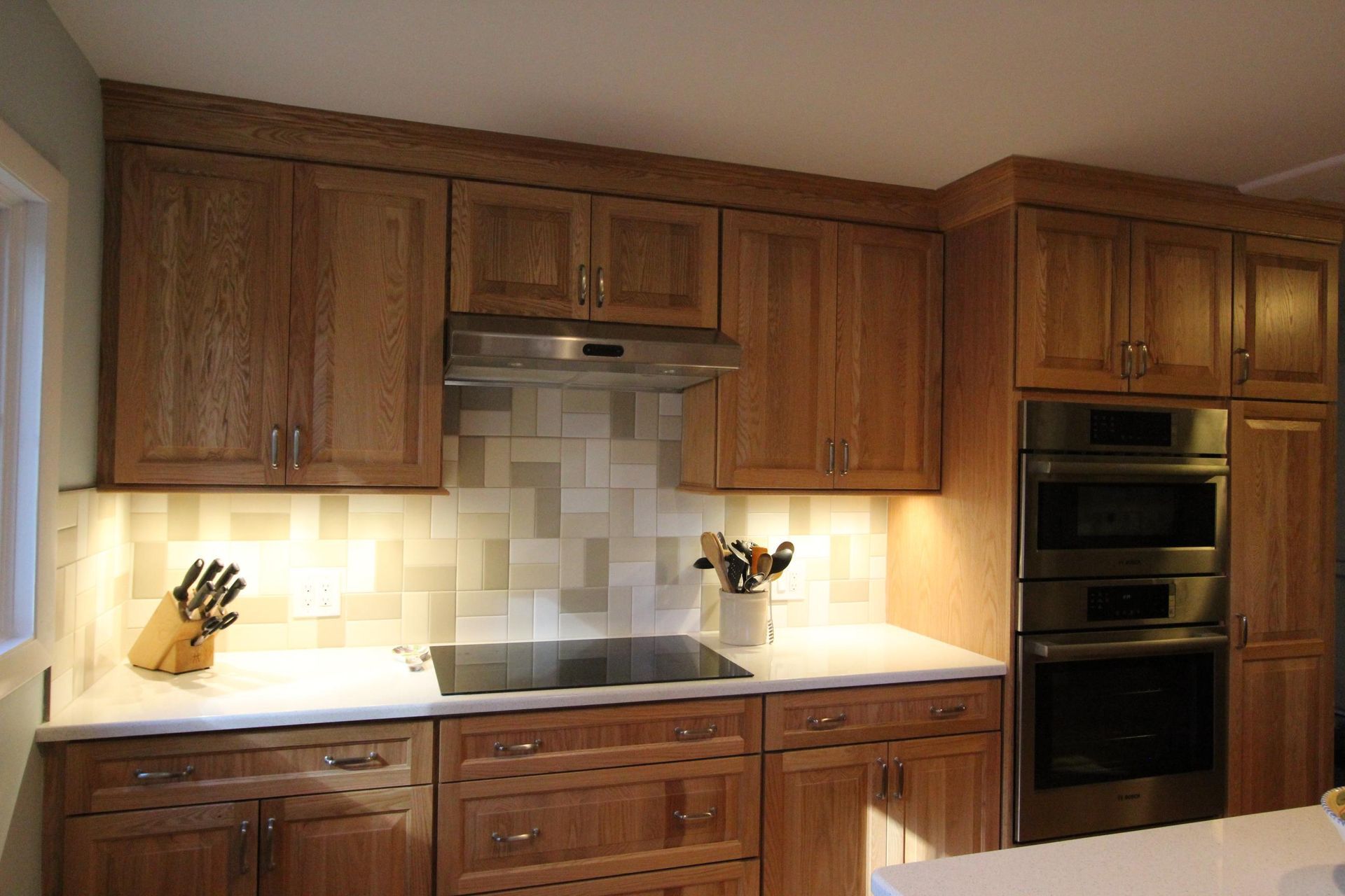 Kitchen with wooden cabinets, white countertops, stove, and tiled backsplash.