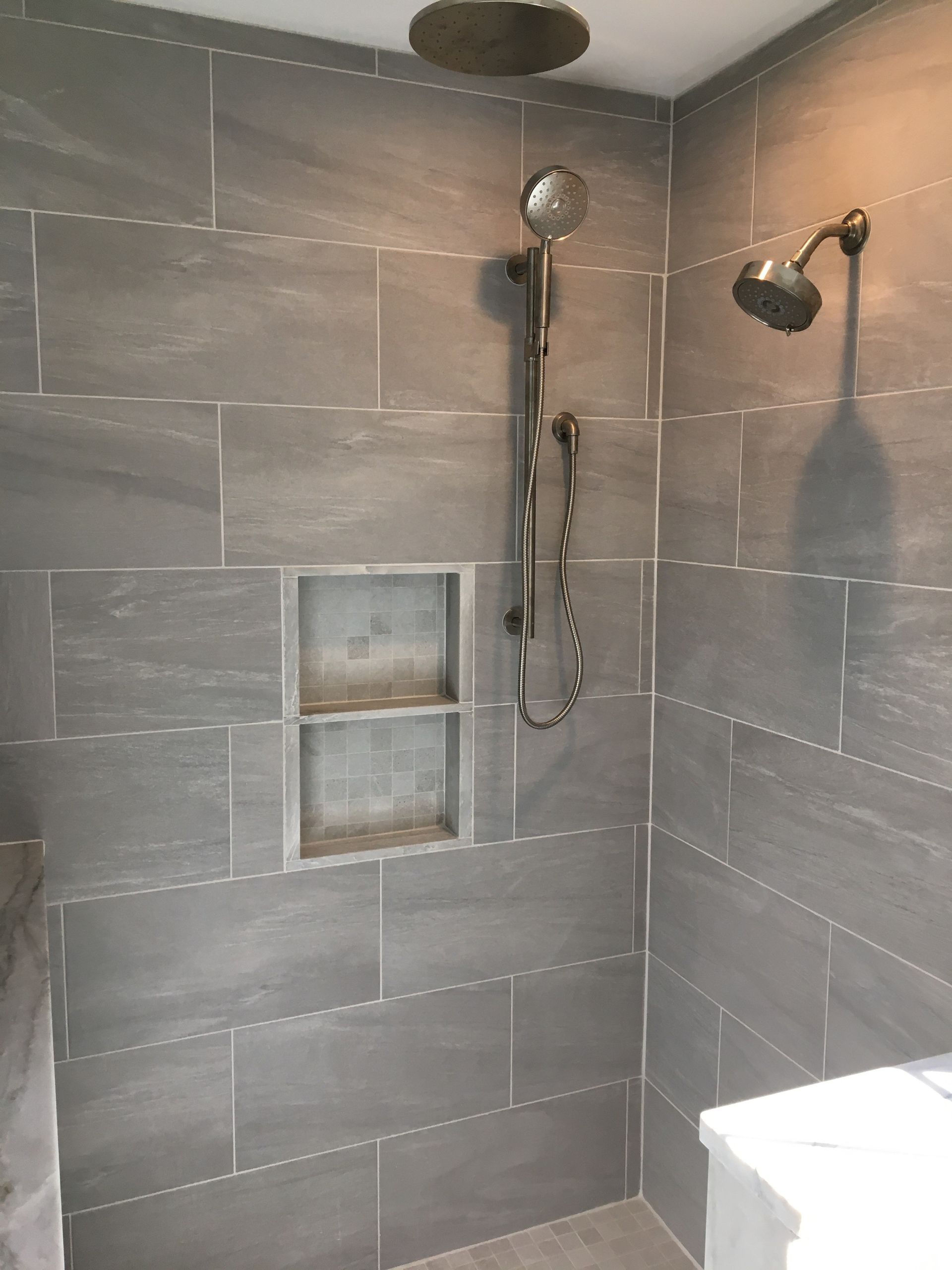 Gray tiled shower with a built-in shelf and two shower heads.