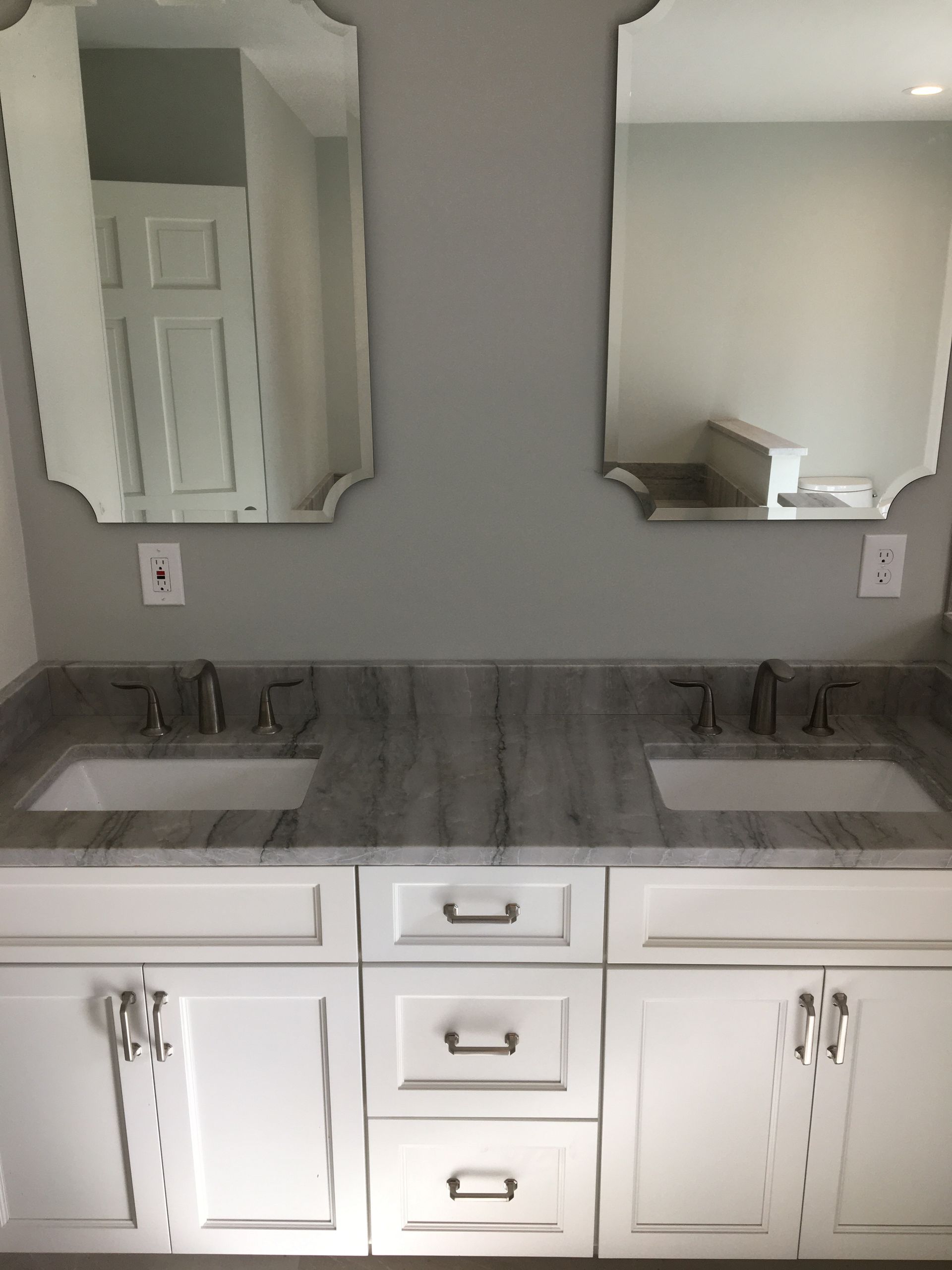 Dual bathroom vanity with gray countertop, white cabinets, and decorative mirrors.