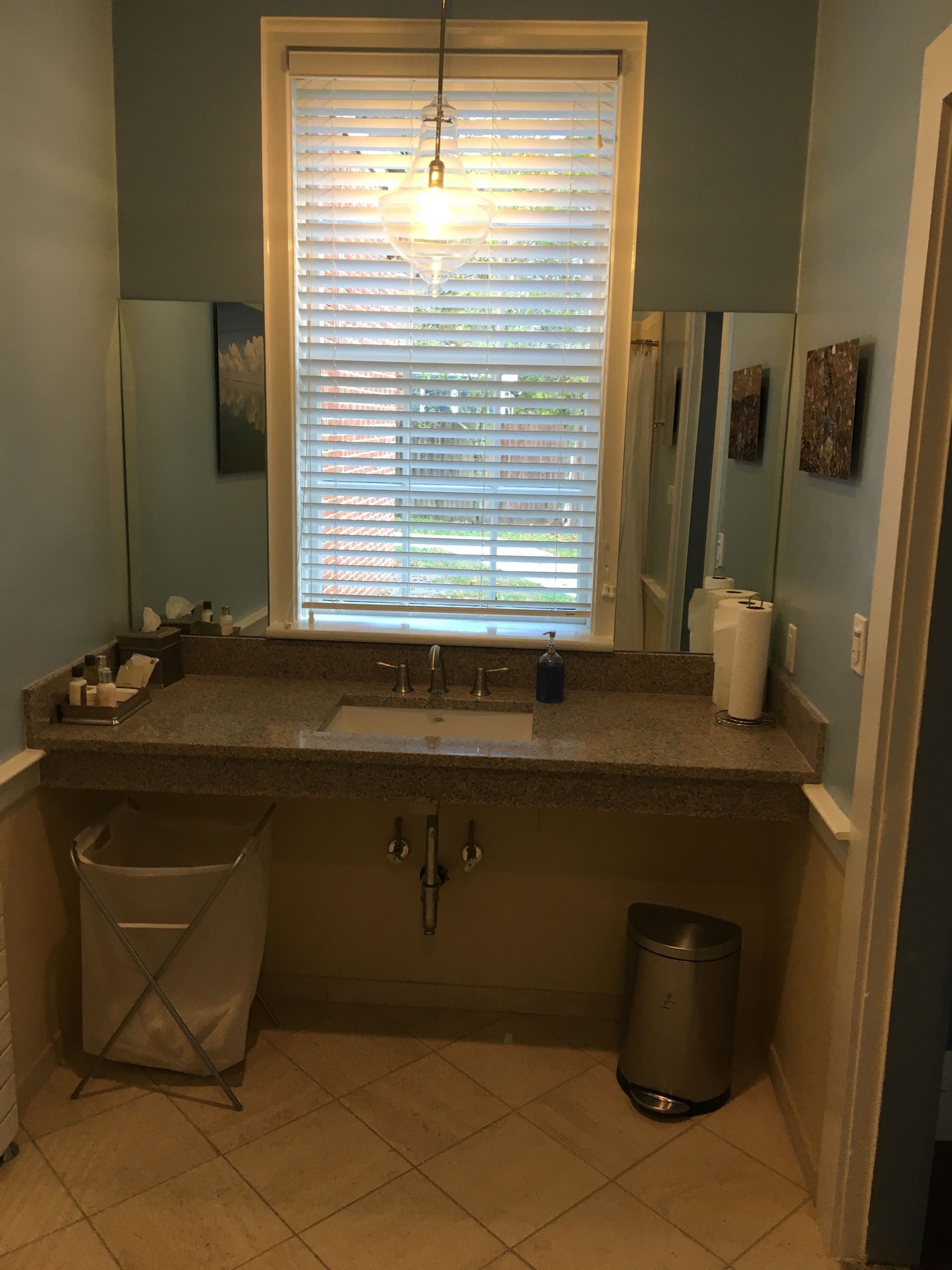 Bathroom with accessible sink, window, and mirror. Light blue walls, granite countertop, and tile floor.