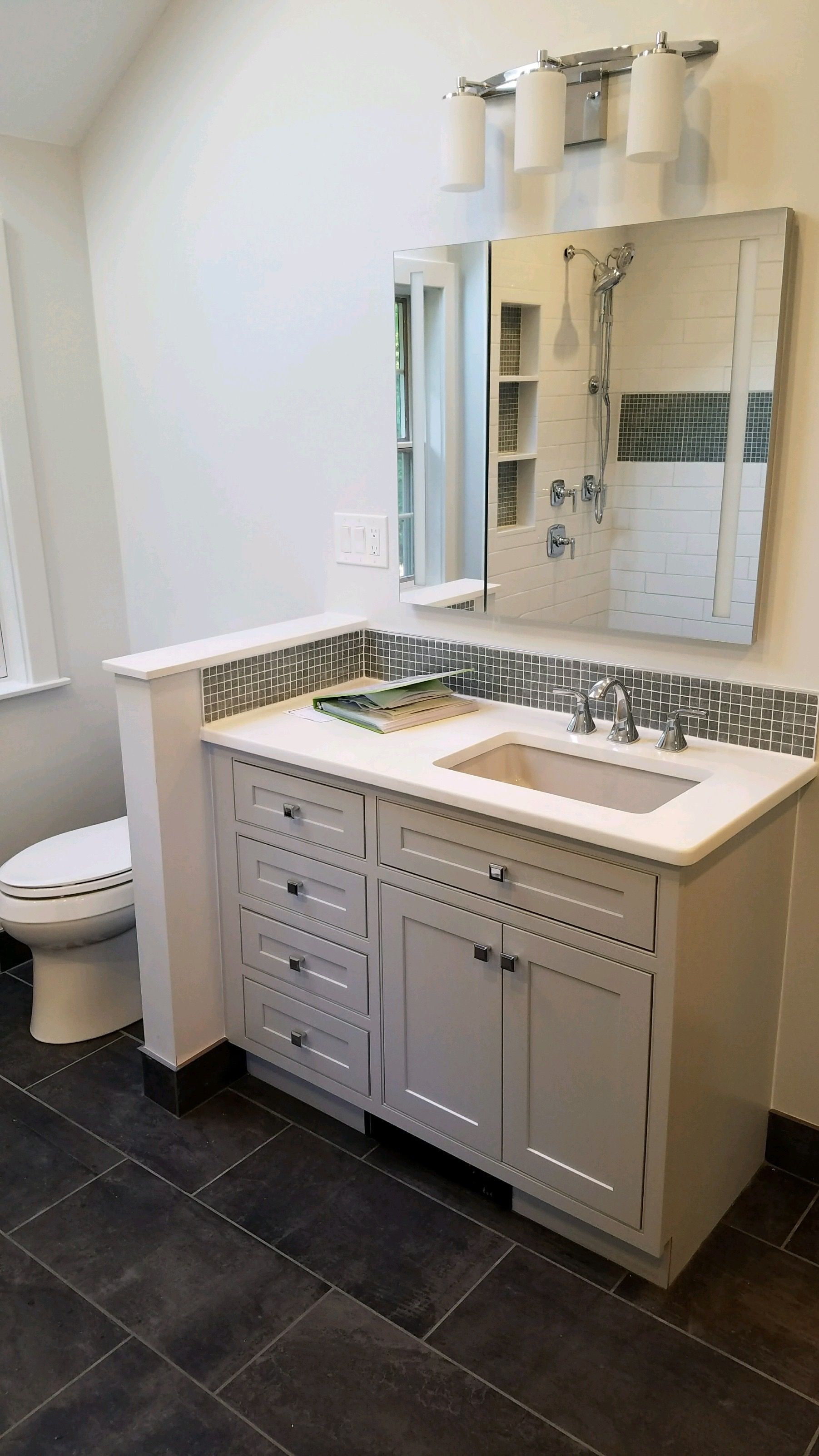 Bathroom with gray vanity, toilet, large mirror, and dark tile floor.