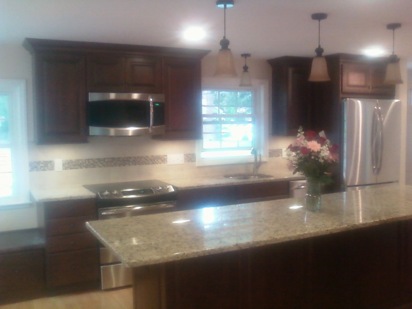 Kitchen with dark wood cabinets, stainless steel appliances, granite countertops, and pendant lights.