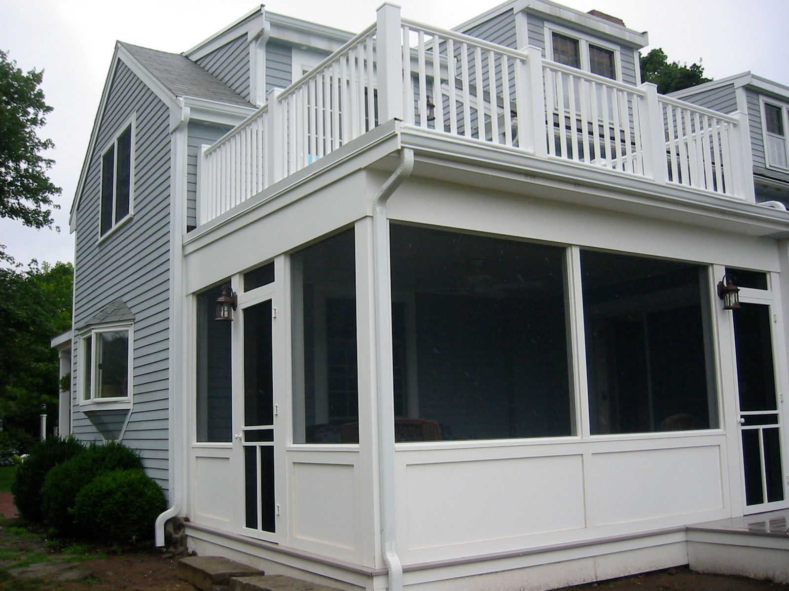 White screened porch attached to a blue house, topped with a balcony.