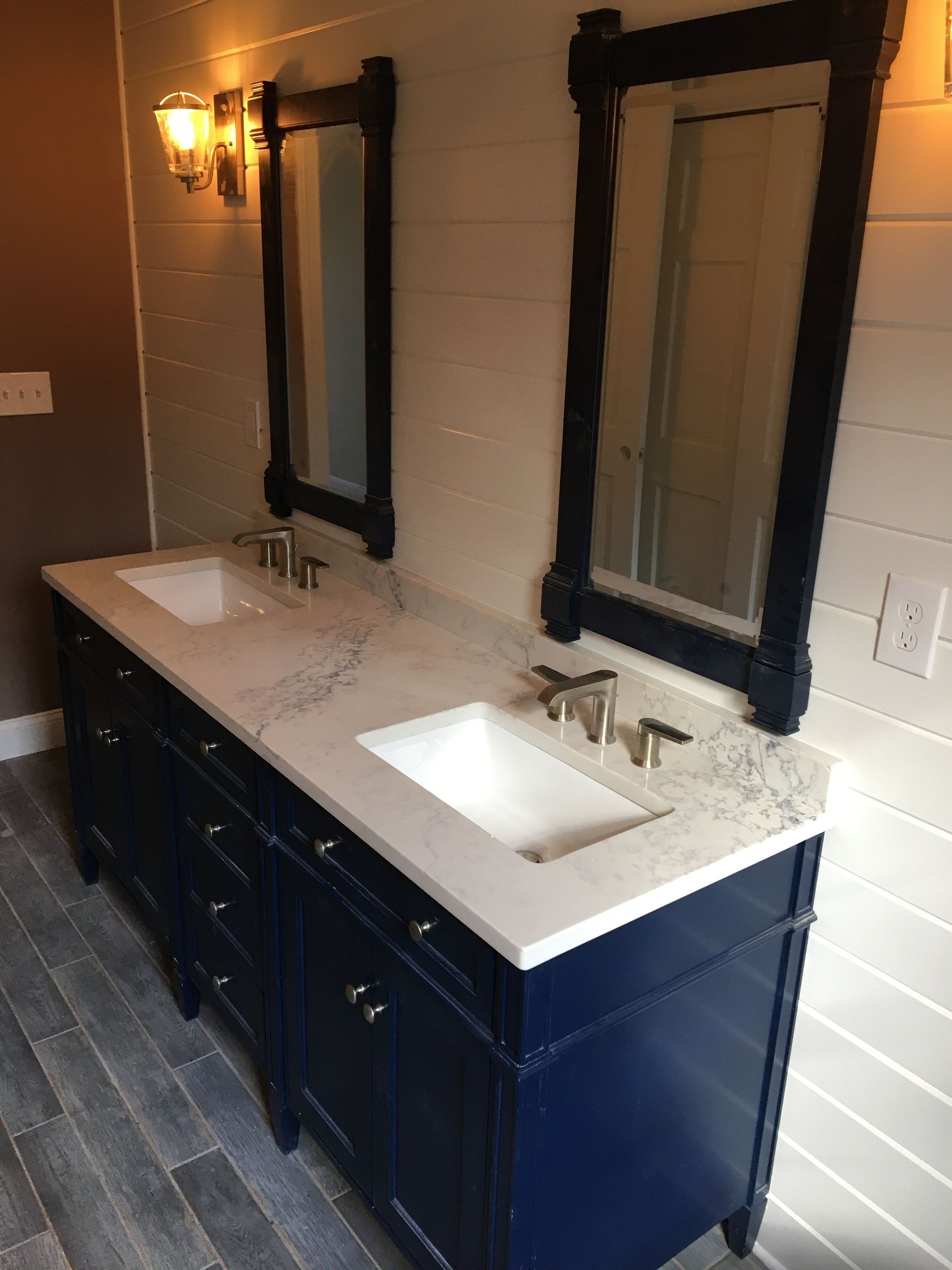 Blue double vanity with white countertop, two mirrors, and wall sconces in a bathroom.