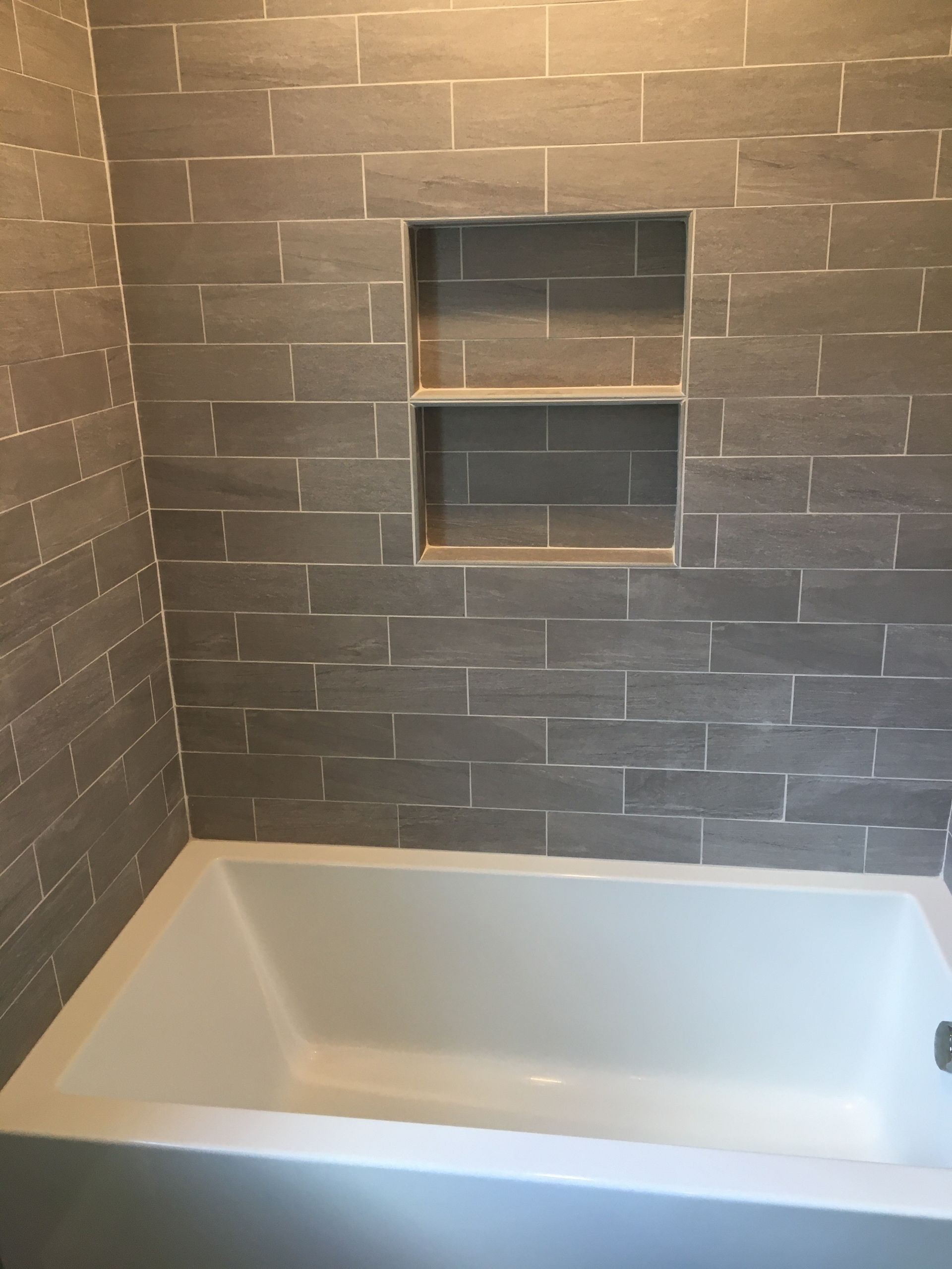 Gray tiled shower surround with a built-in shelf above a white bathtub.