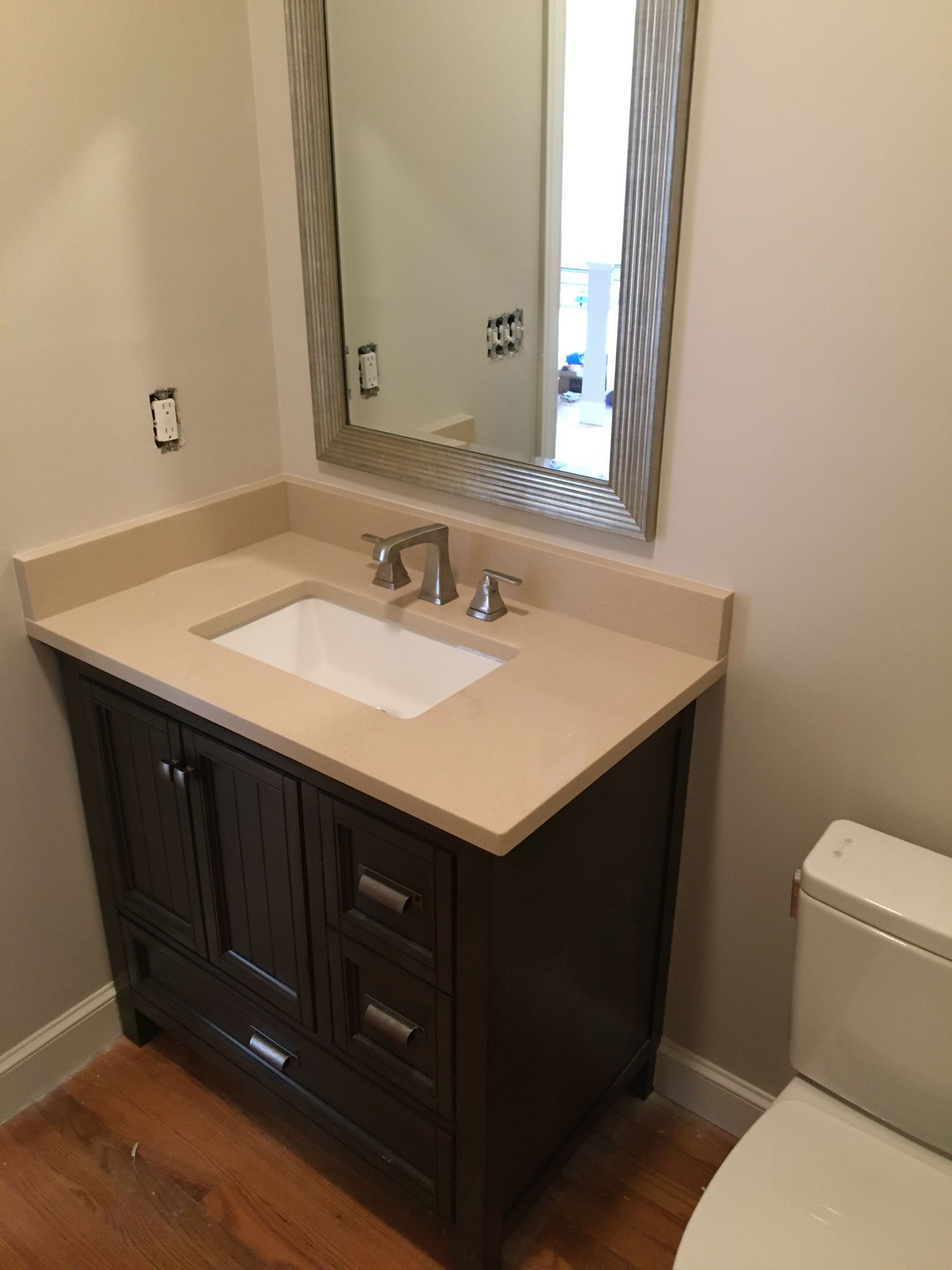 Dark brown vanity with beige countertop, white sink, and silver faucet in a bathroom with a mirror.