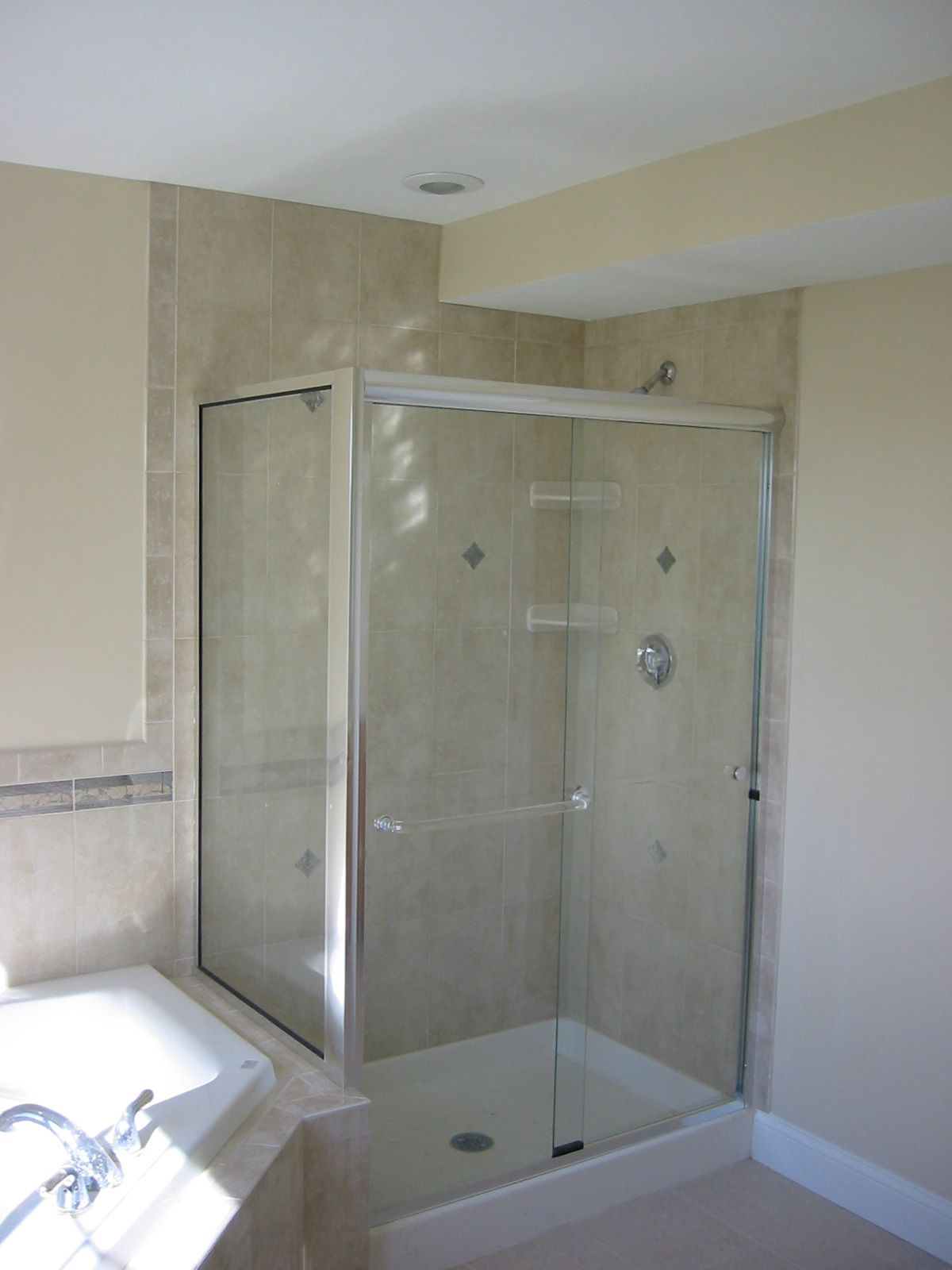 Corner glass shower with beige tiled walls and a white base.