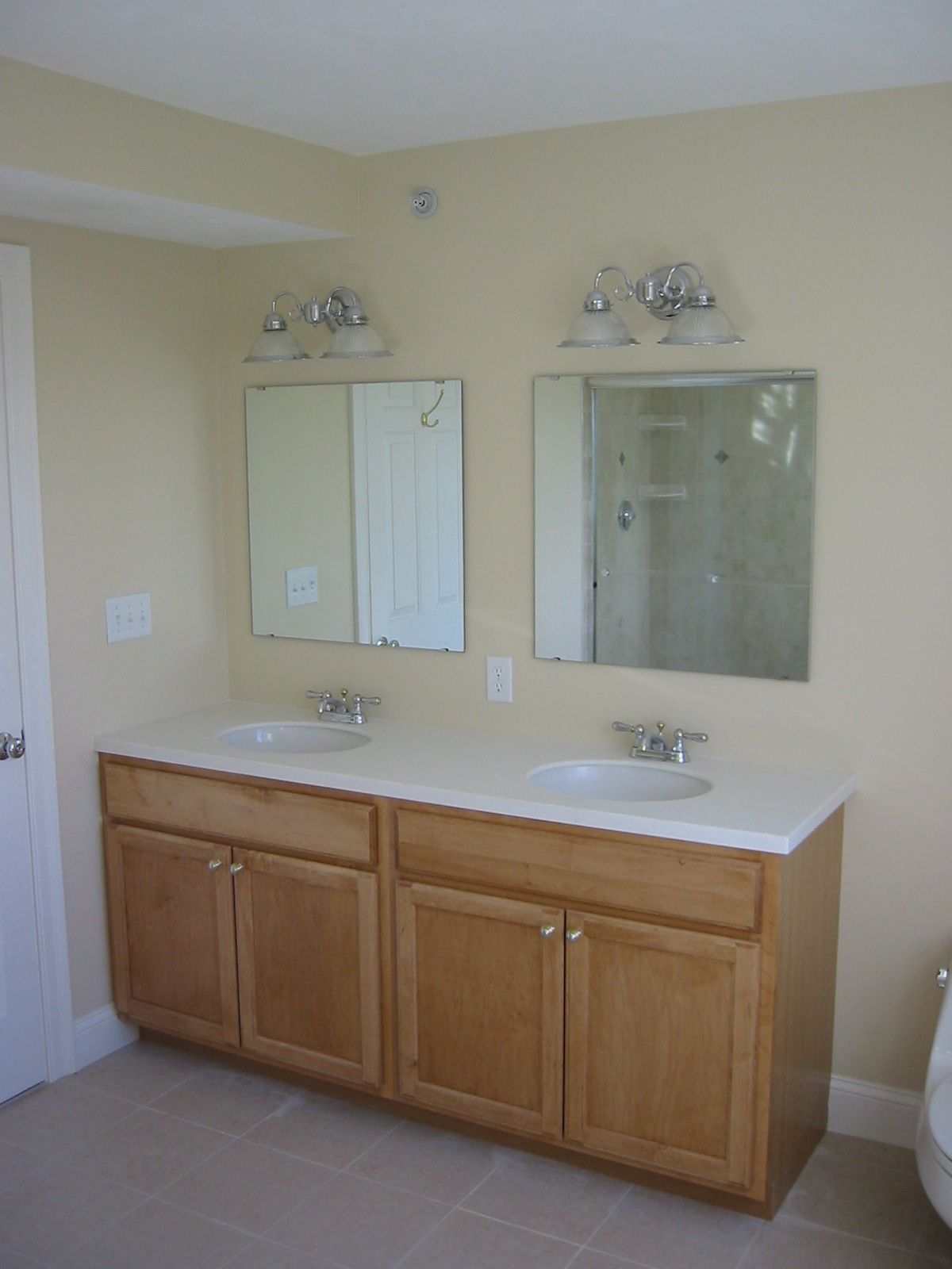 Bathroom with a double vanity; light wood cabinets, two sinks, two mirrors, and beige walls.