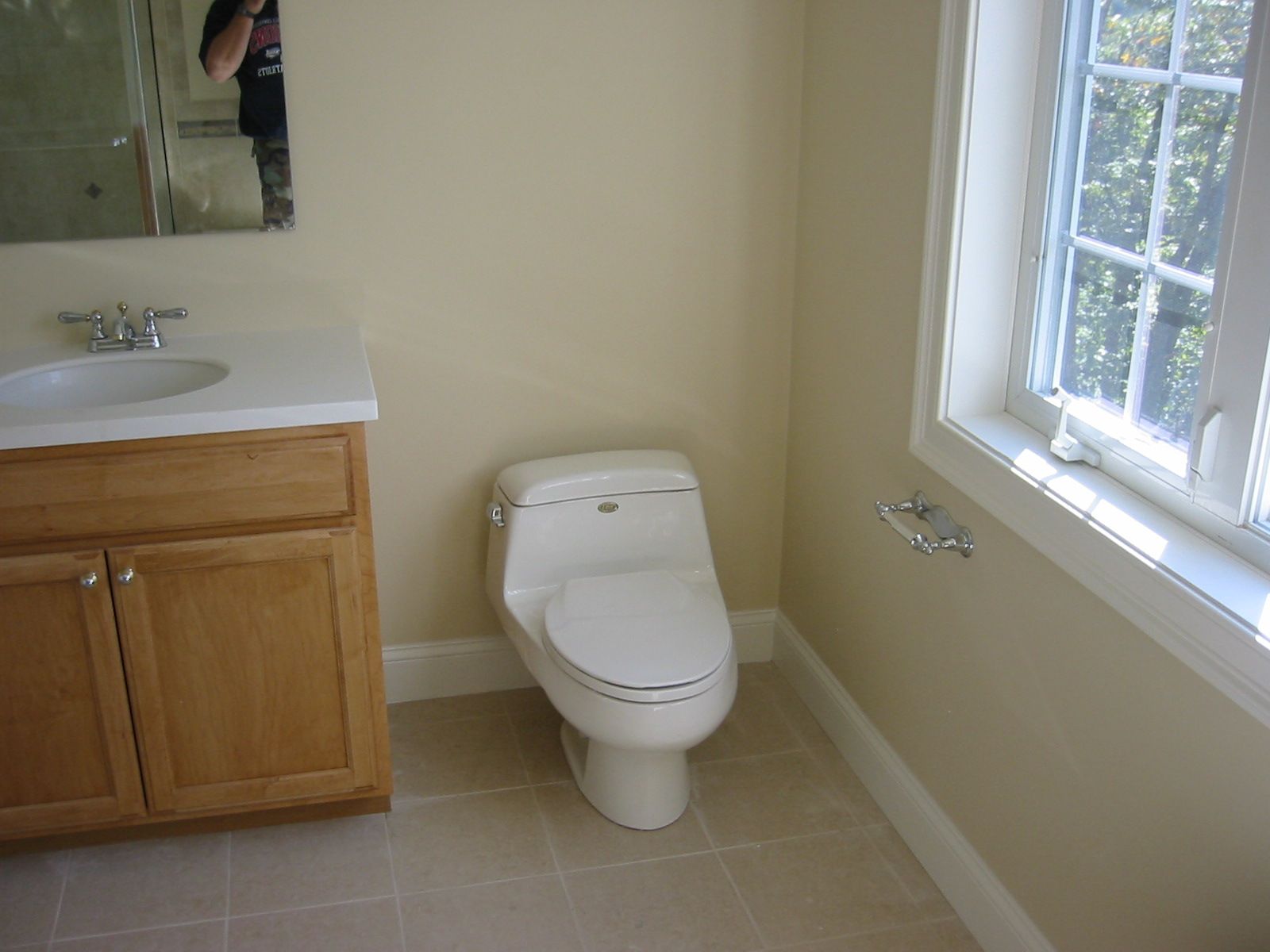 Bathroom with toilet, vanity, and window. Neutral walls, light-colored cabinets, and a tiled floor.