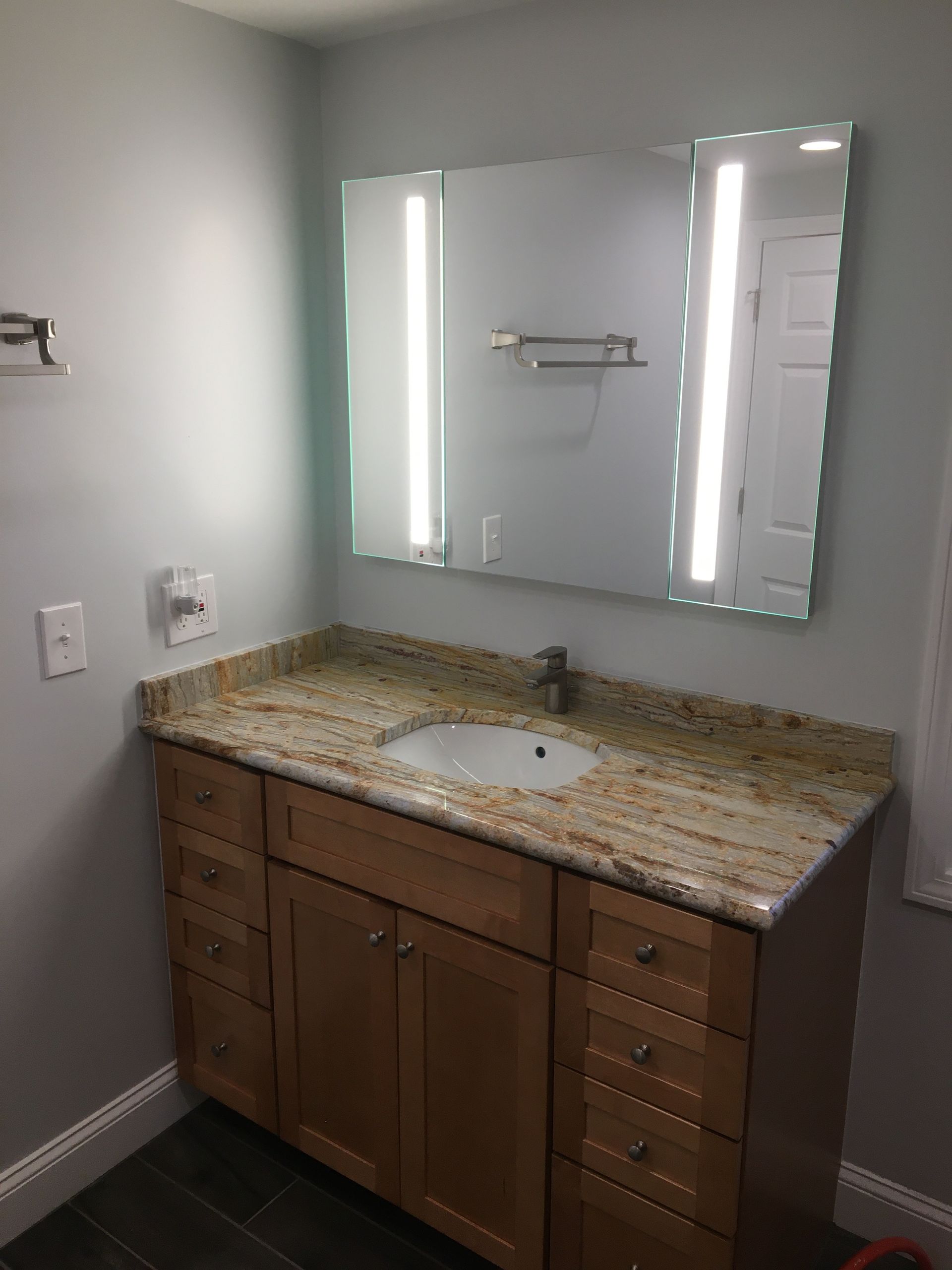 Bathroom with a light wood vanity, granite countertop, oval sink, and large mirror with side lights.