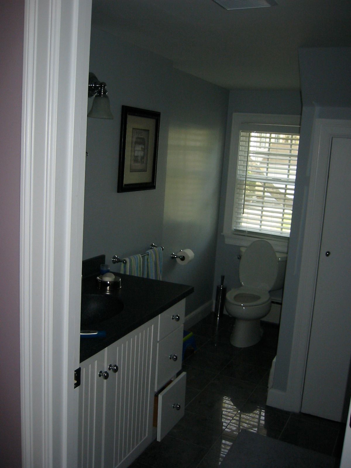 Bathroom with a vanity, toilet, and window; walls are blue, cabinet white, and floor dark.