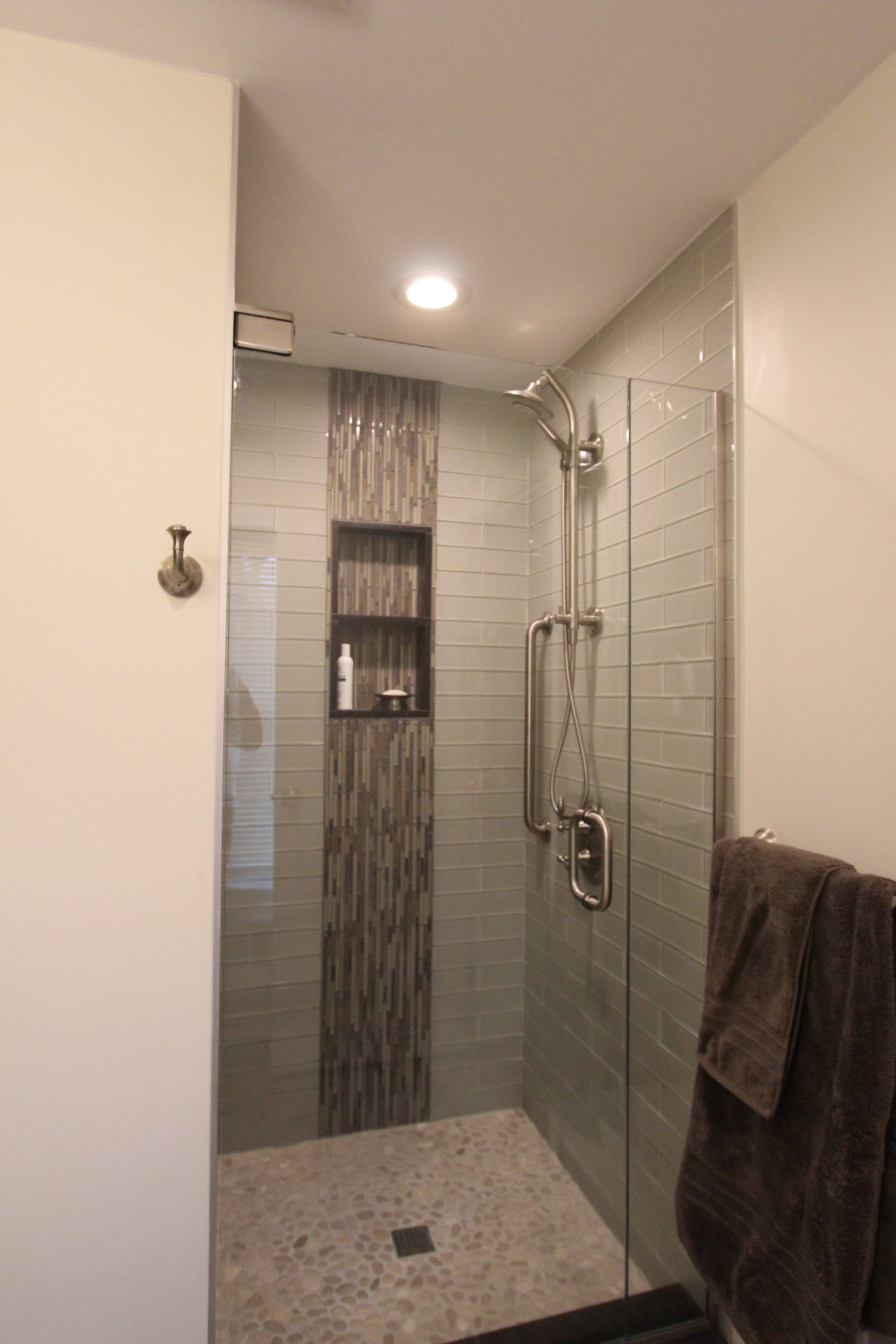 Shower with glass door, built-in shelf with products, and towel rack with brown towels.