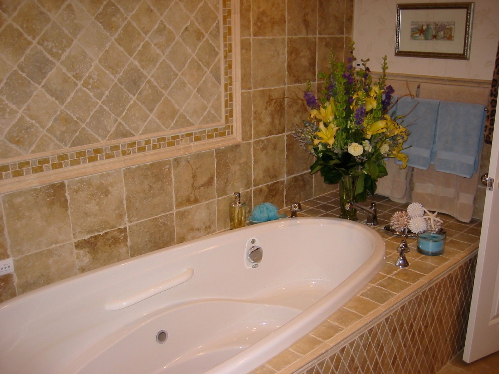 Luxurious bathroom with a white tub, floral arrangement, and tan tiled walls.