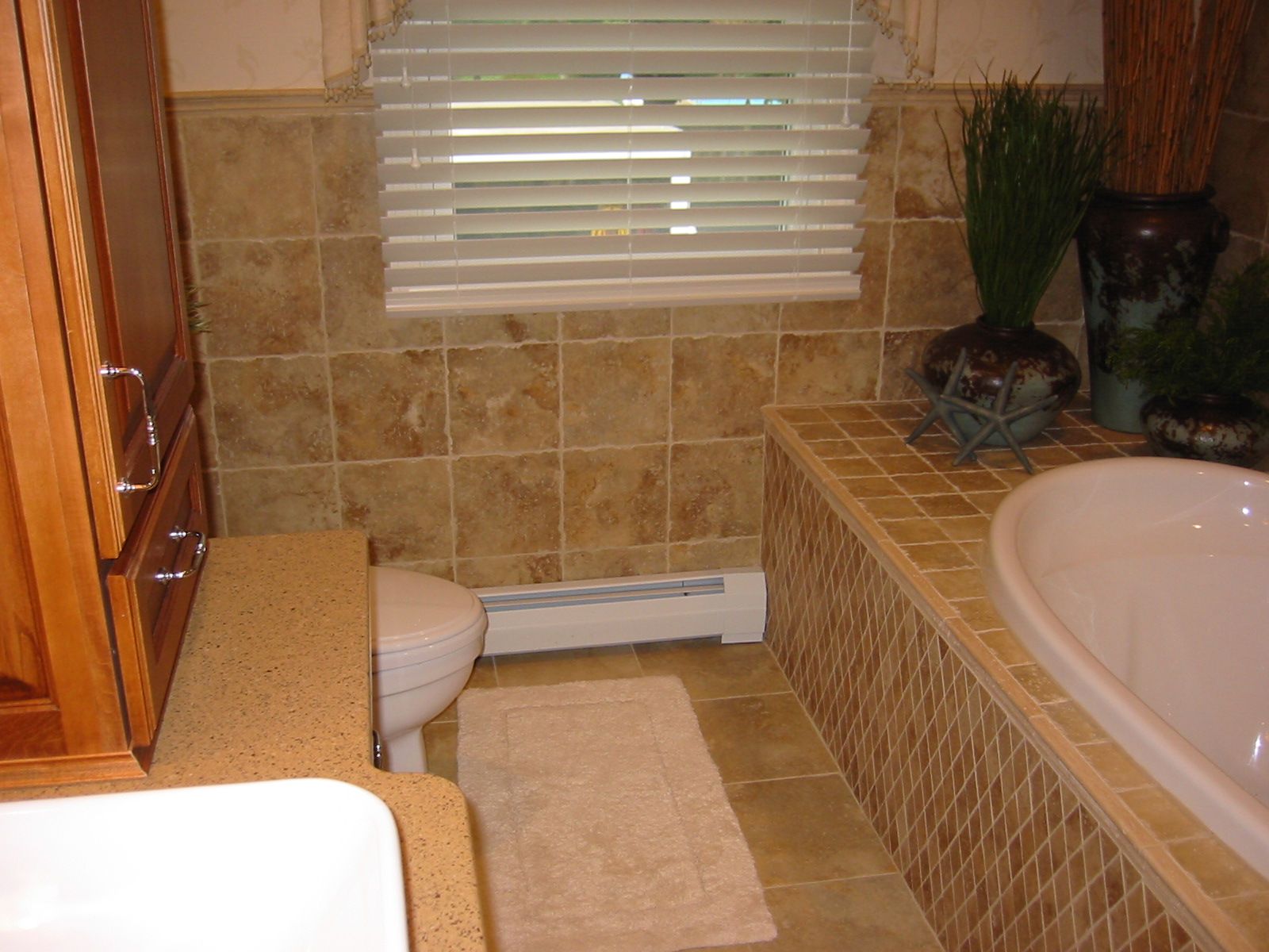 Bathroom with tile walls, toilet, bathtub, cabinet, and window with blinds.