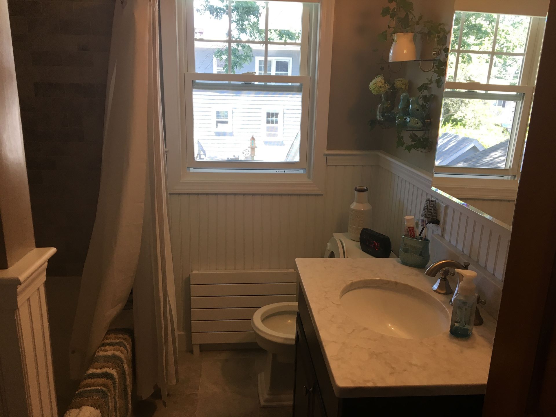 Bathroom with a sink, toilet, two windows, and white paneling.