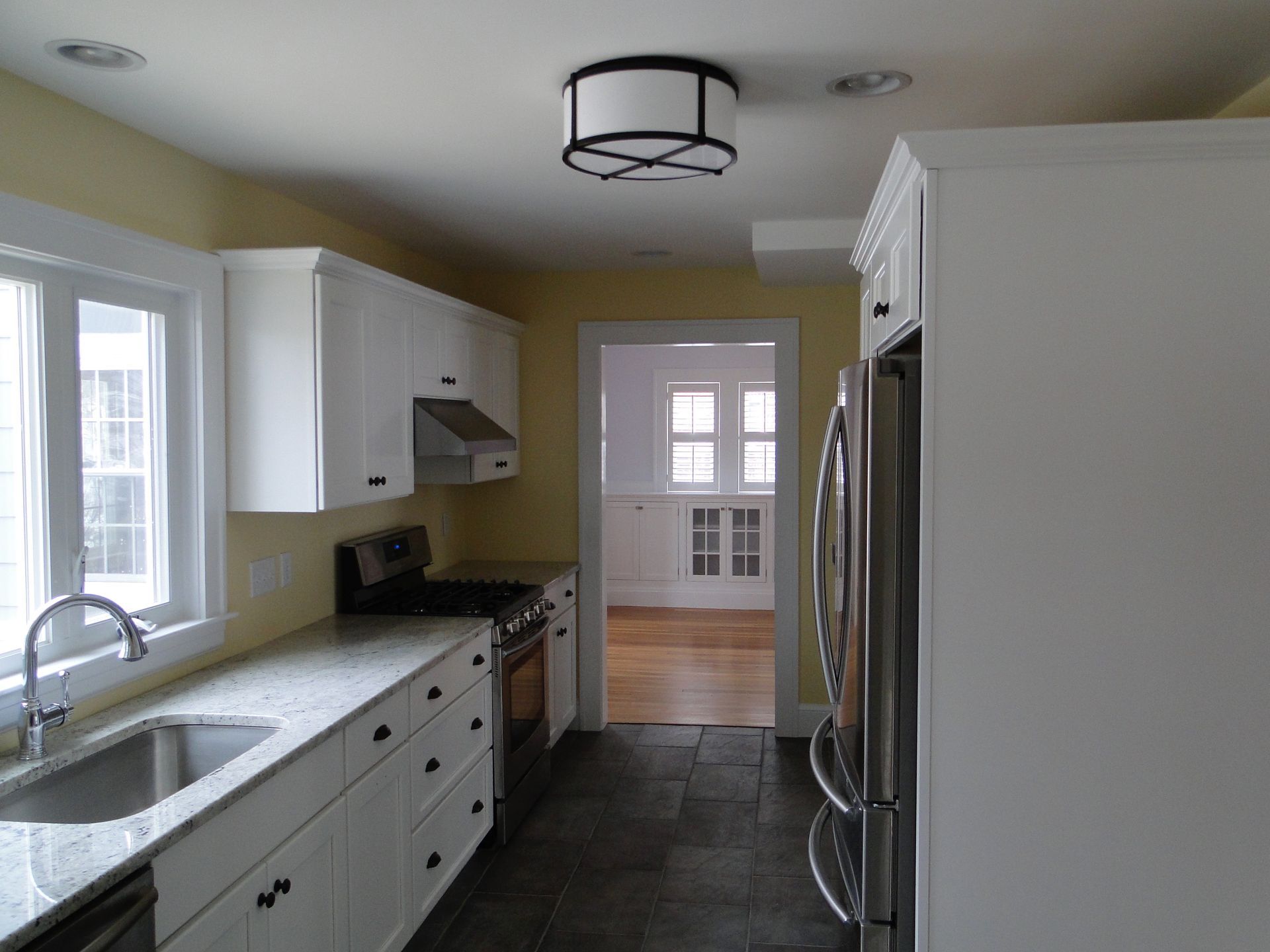 White kitchen with granite countertops, stainless steel appliances, and a view into another room.