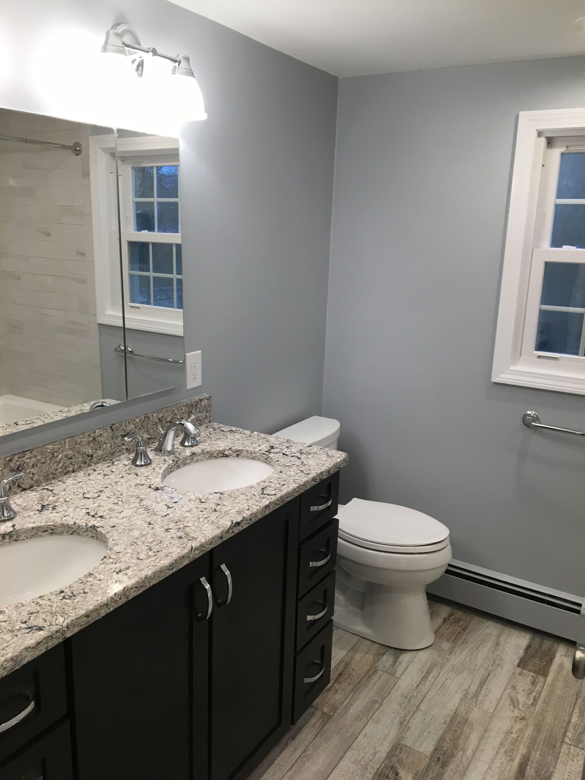 Bathroom with double sink vanity, toilet, window, grab bar, and light gray walls.