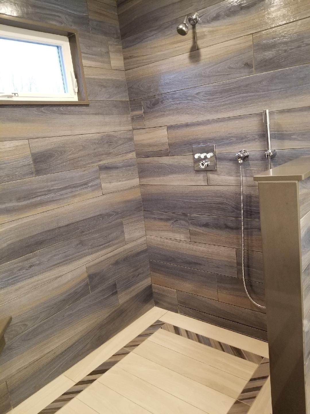 Shower with blue-grey horizontal wood-look tile, light floor tile with dark border, and a window.