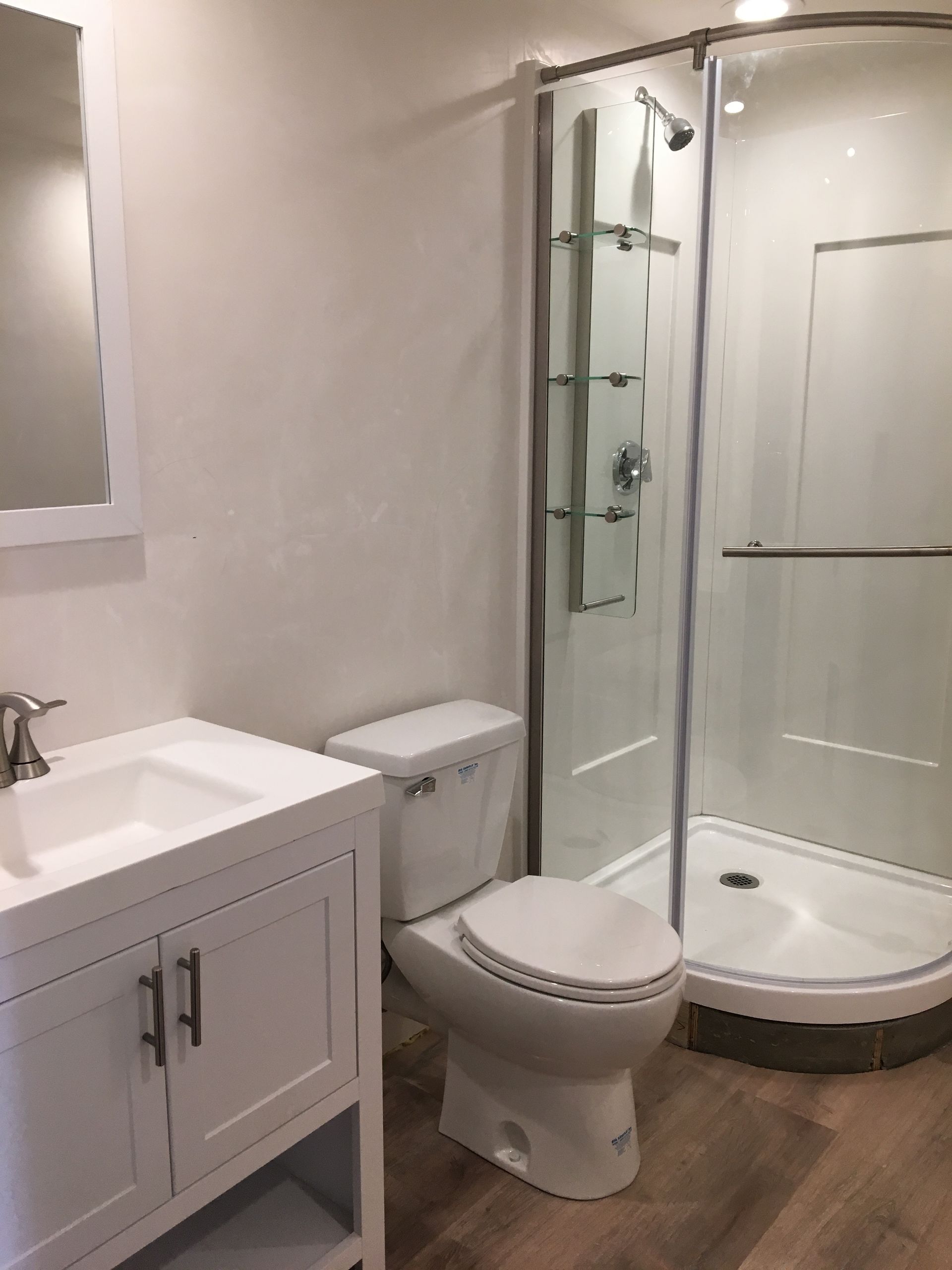 Bathroom with white vanity, toilet, and curved shower. Light wood-look floor.