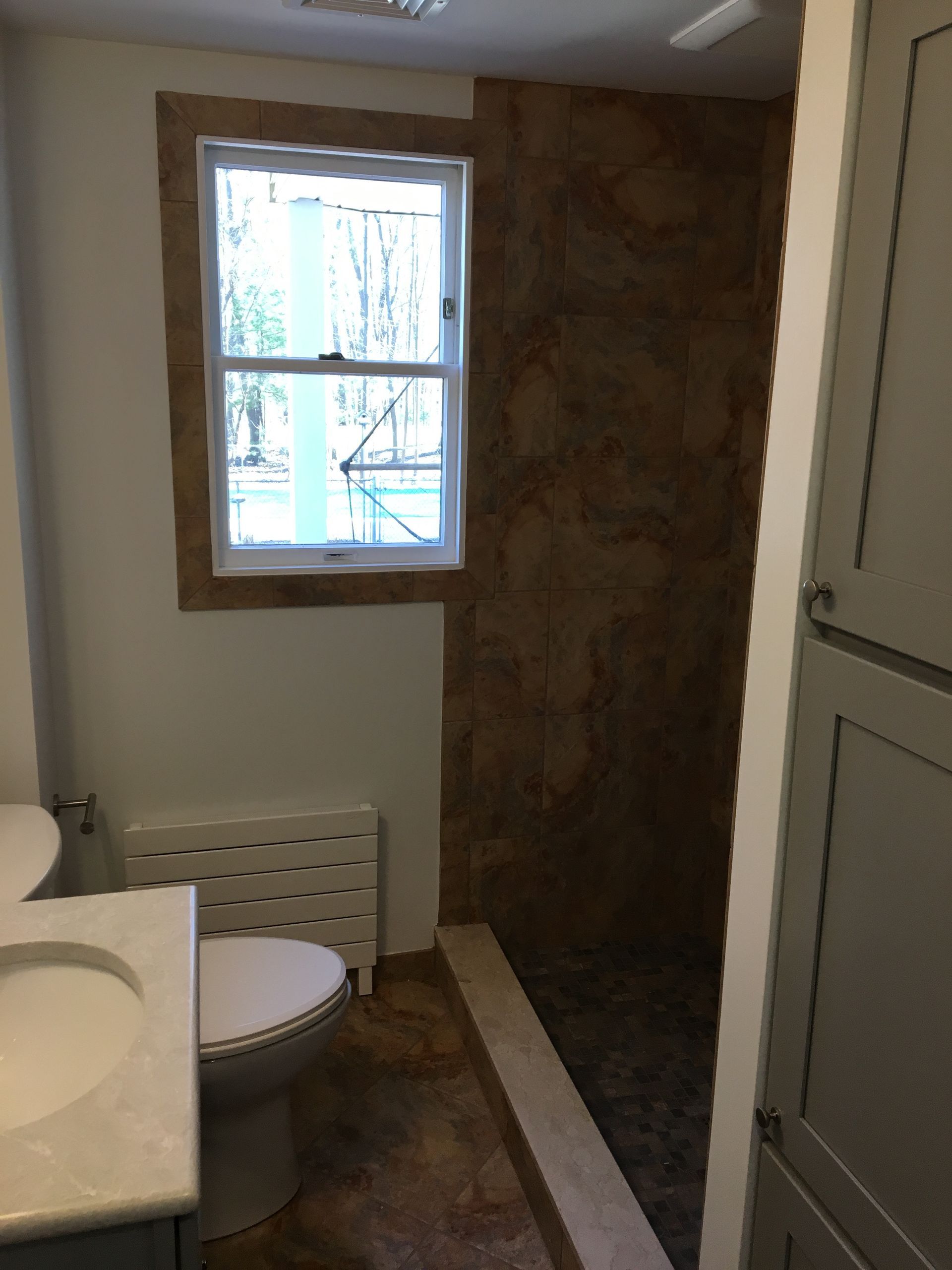 Bathroom with a window, toilet, and shower with brown stone wall.