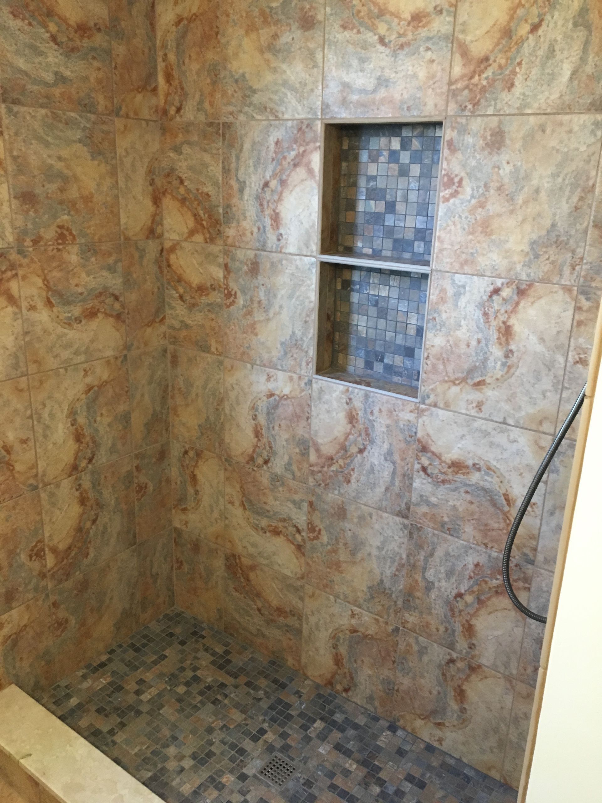 Shower with brown and beige marbled tiles, dark blue mosaic floor, and a built-in shelf with blue mosaic tiles.