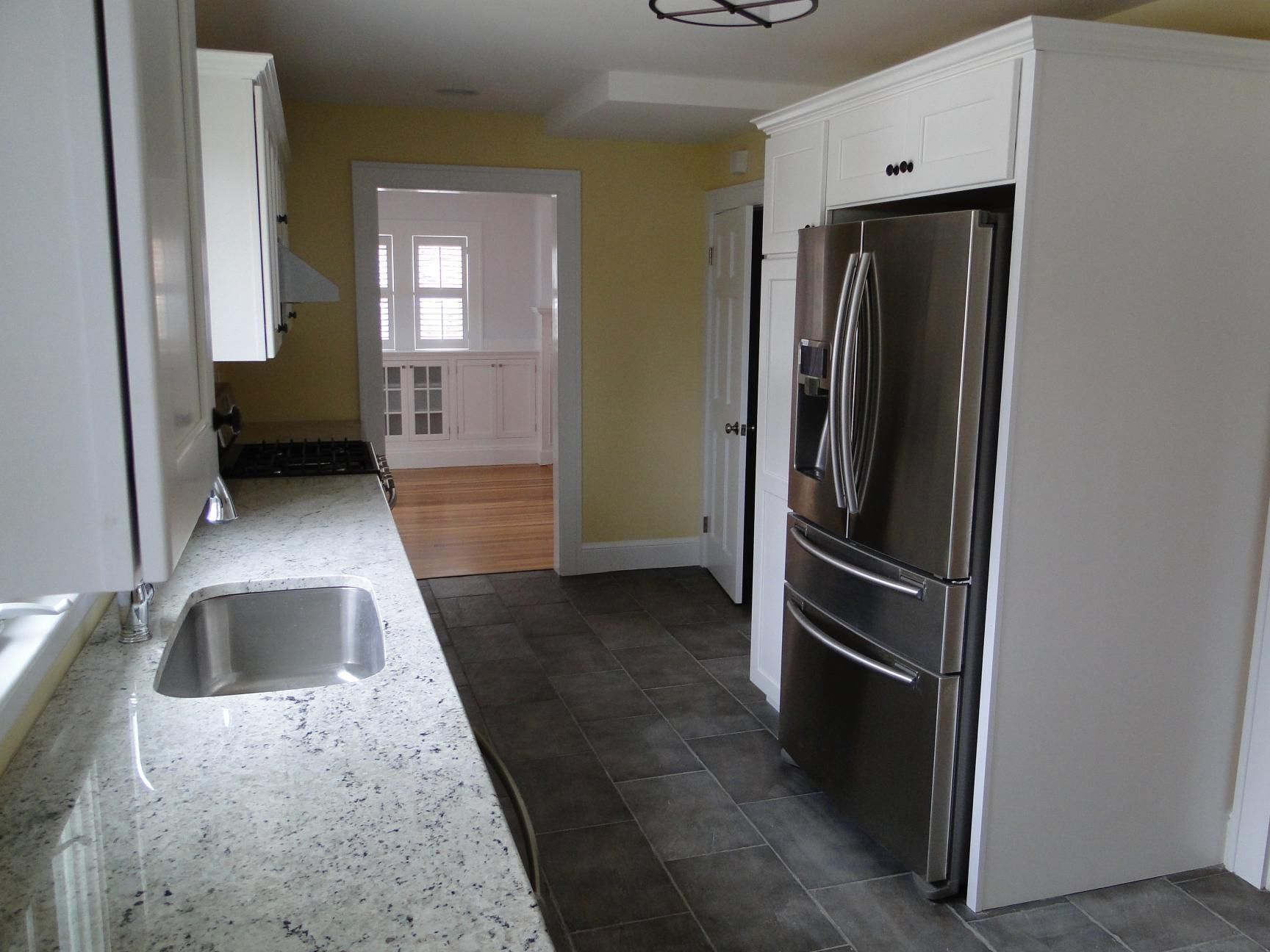 Kitchen with white cabinets, stainless steel fridge, granite countertop, and a doorway to another room.
