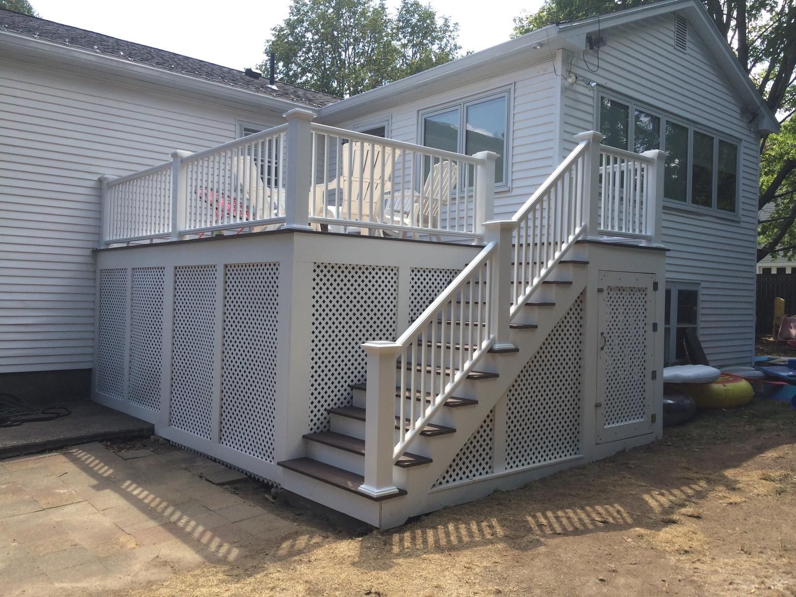 Deck with white railing, lattice siding, and stairs attached to a two-story house.