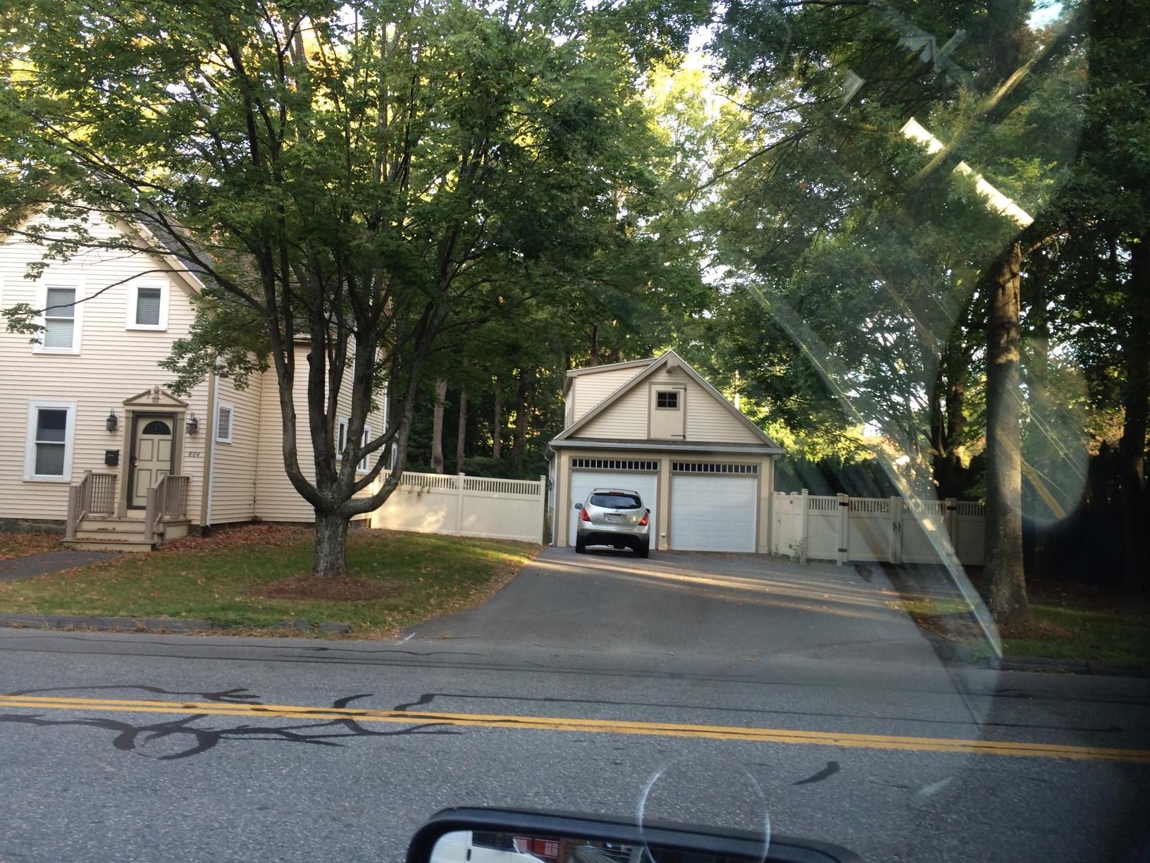 A beige house and a two-car garage with a car parked in the driveway on a sunny day.