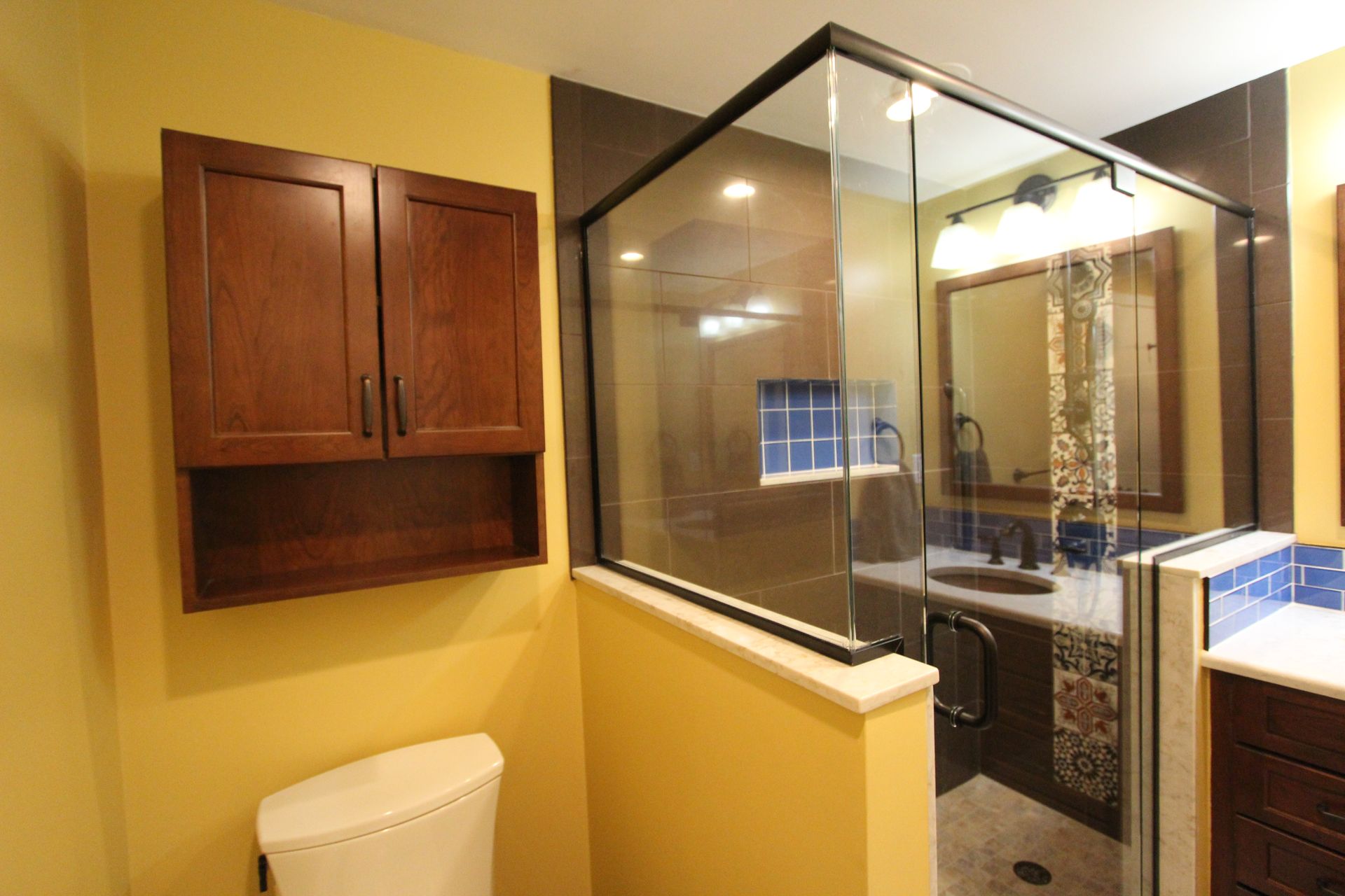 Bathroom with a glass shower, dark brown cabinets, and yellow walls.