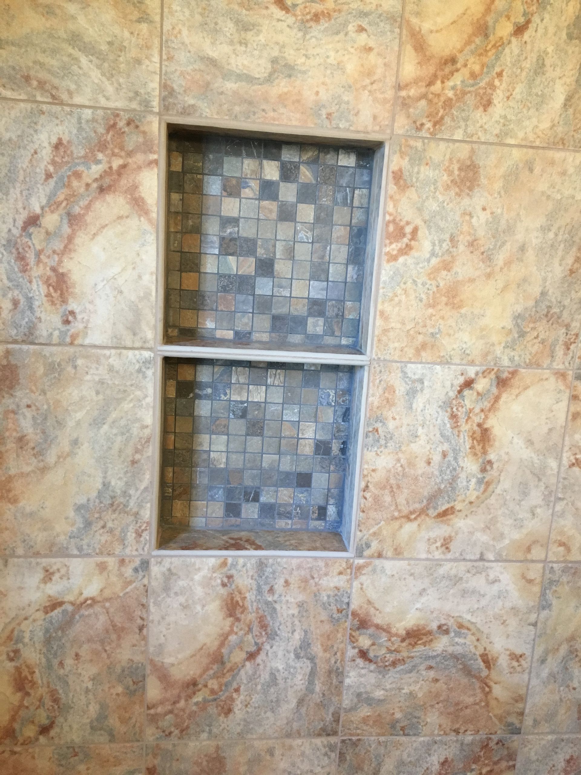 A shower niche with gray mosaic tile inside the recess, surrounded by brown and tan patterned square tiles.