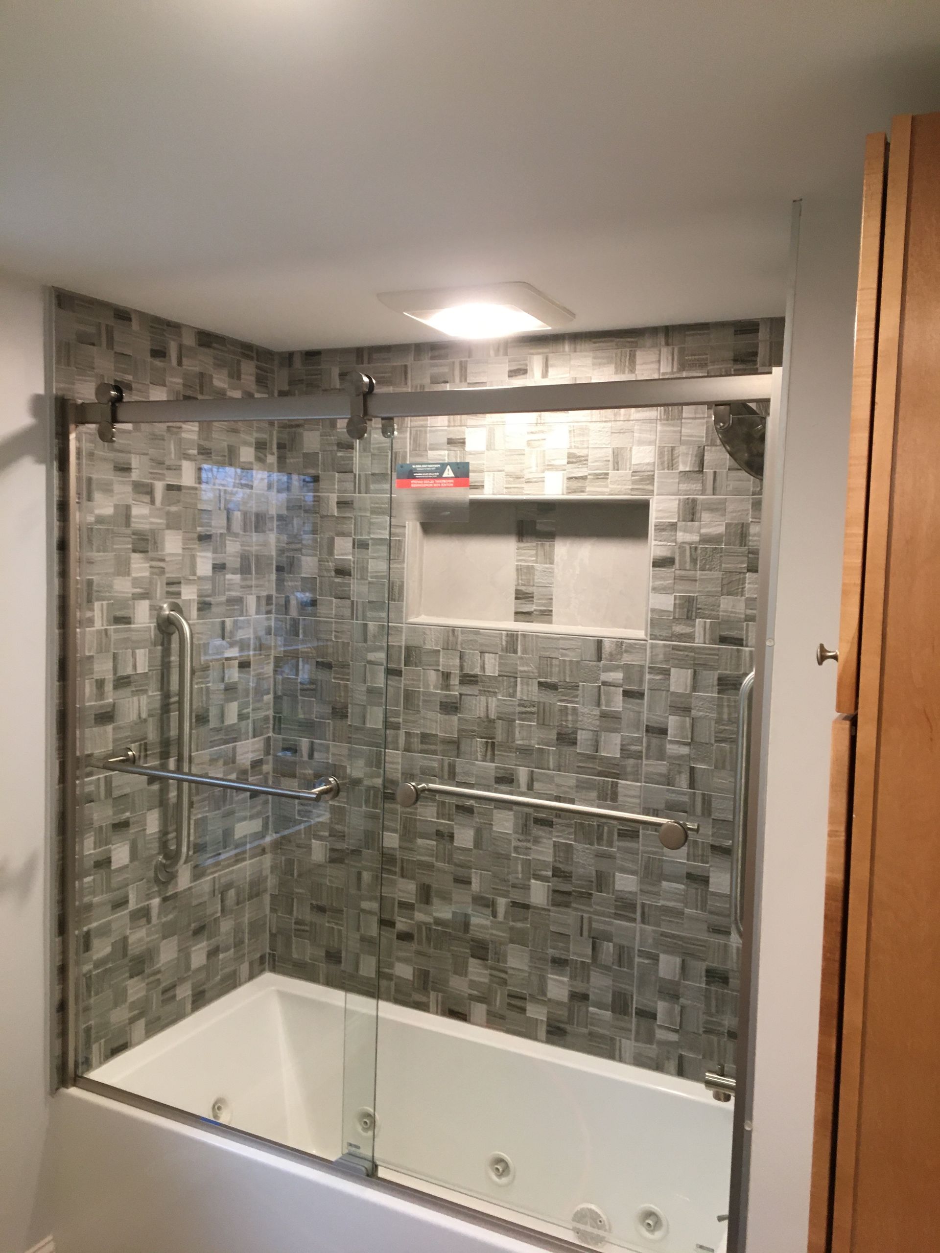 Shower stall with glass doors, tiled walls in gray tones, built-in niche, and silver hardware.