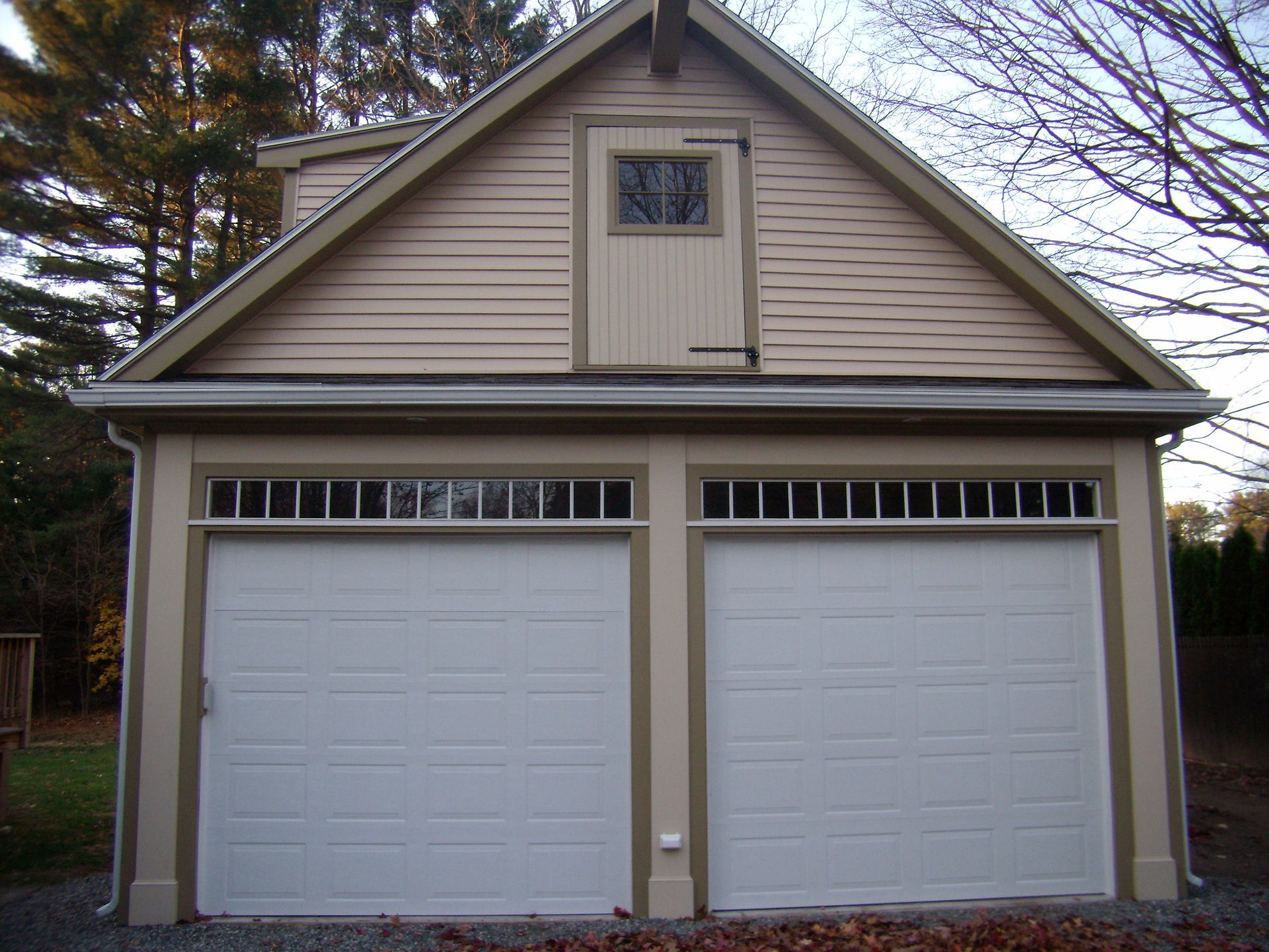 Two-car garage with white doors, tan siding, and a small window above.
