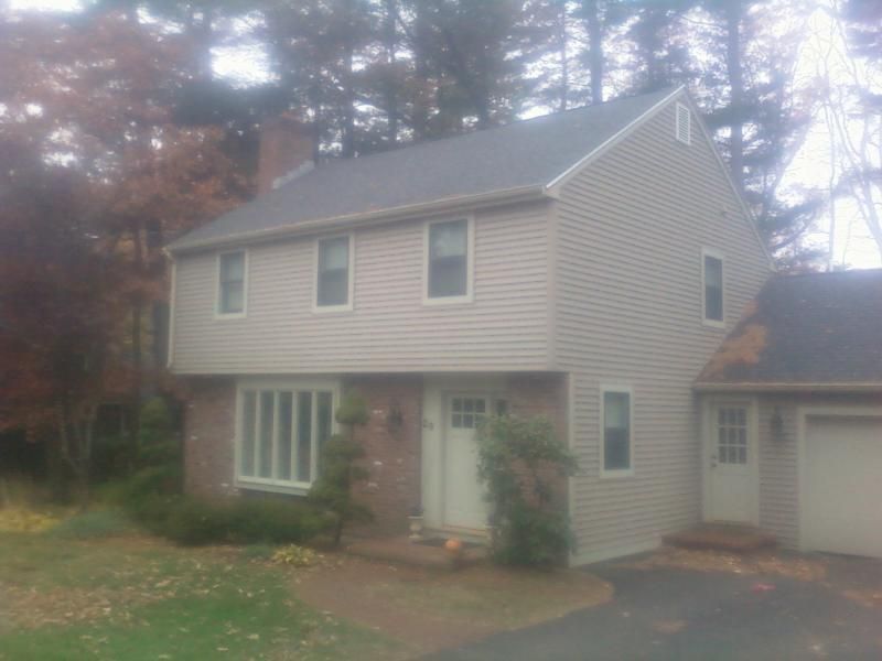 Two-story house with beige siding, brick front, and attached garage; autumn foliage.