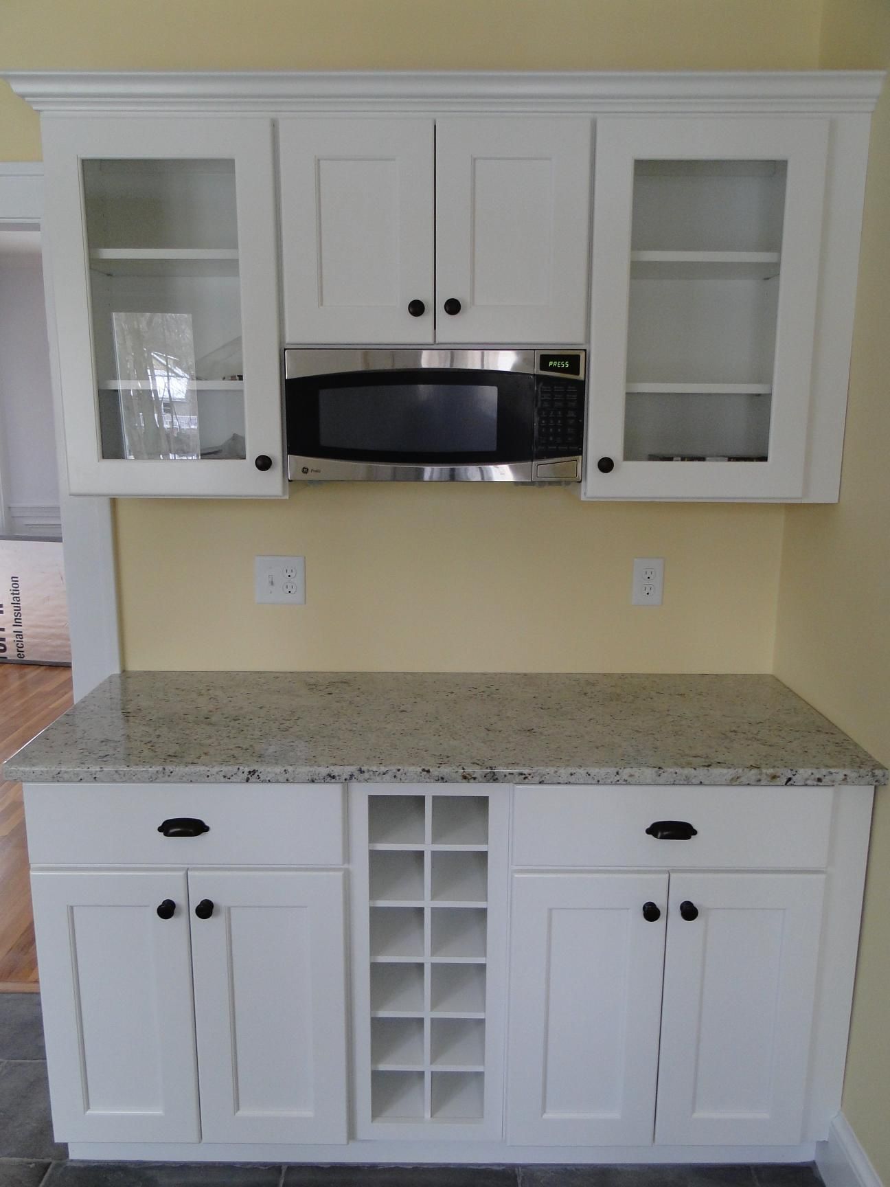 White kitchen cabinets with a microwave, wine rack, and granite countertop.