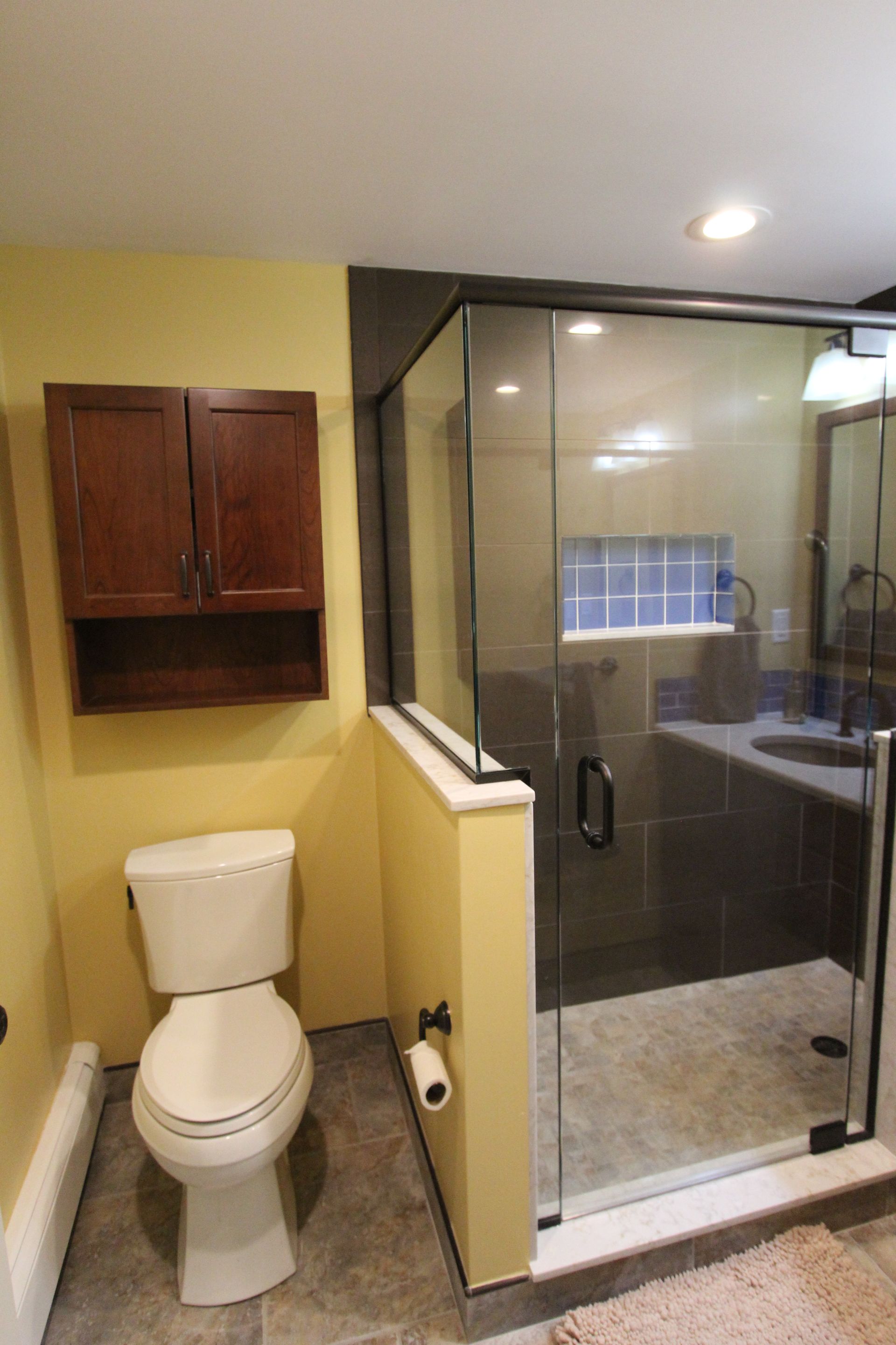 Bathroom with a toilet, cabinet, shower, and vanity. Yellow walls and gray tile flooring.